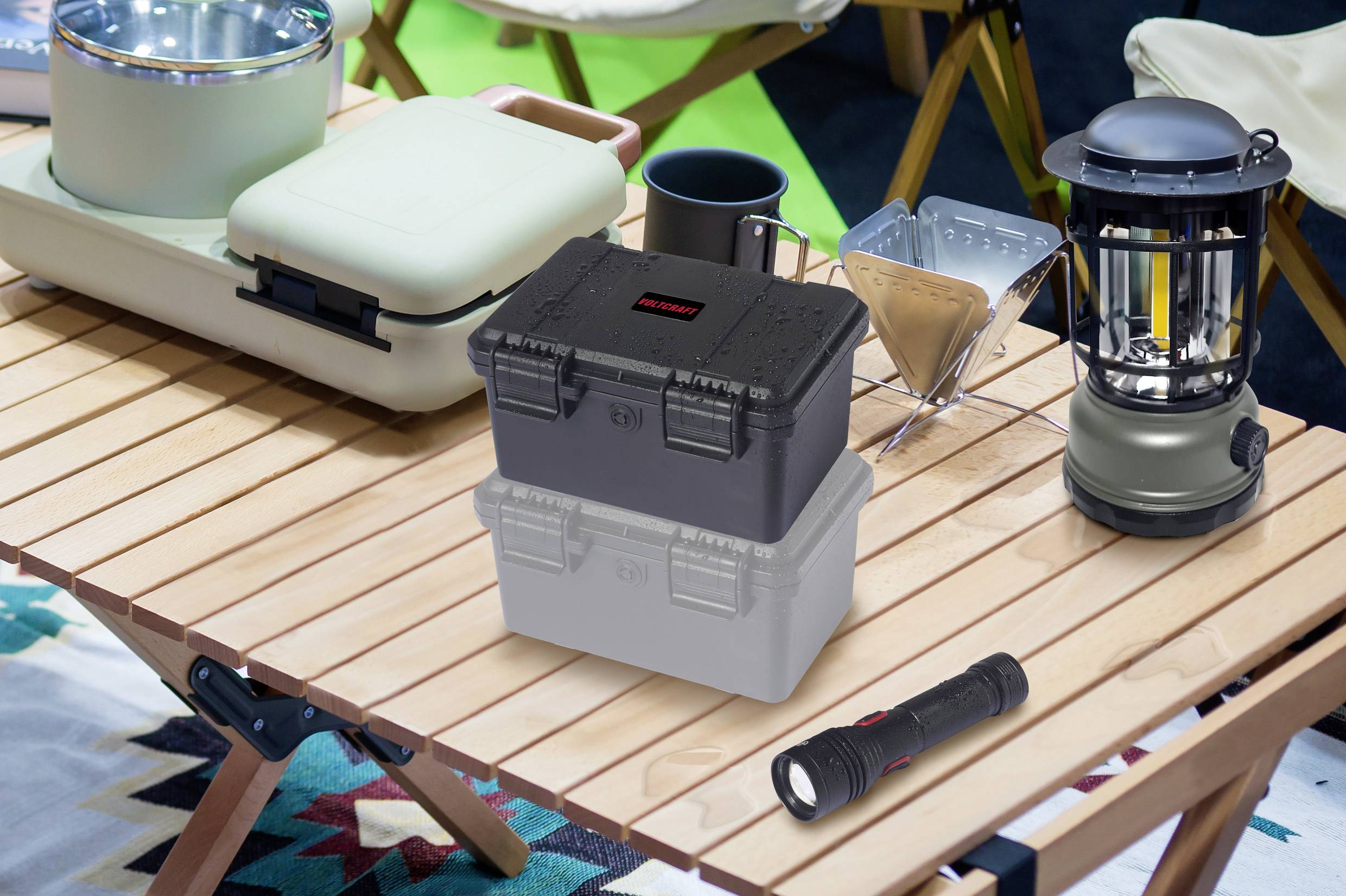 Kampingtisch mit Geschirr, Taschenlampe und Laterne, im Freien aufgestellt. Der Tisch steht auf einem gemusterten Teppich.