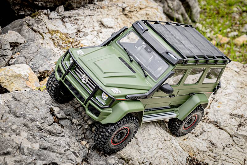 RC-Modellauto im robusten, geländegängigen Design, fährt über felsiges Gelände. Fahrzeug ist in Olivgrün mit Dachträger gestaltet.