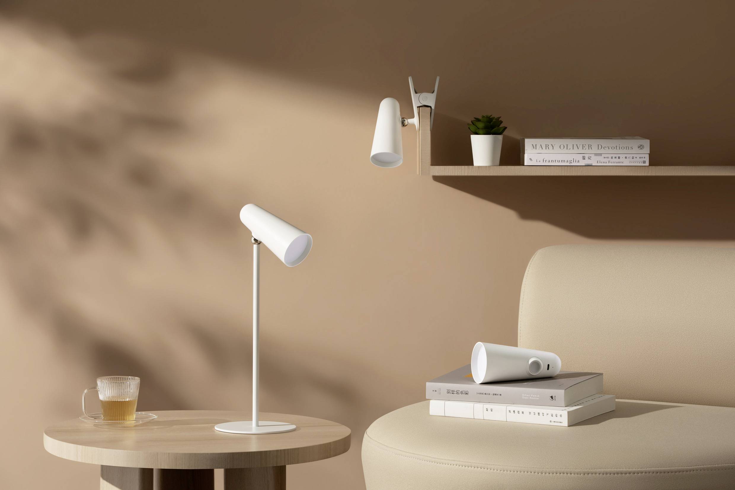 Ein minimalistisches Wohnzimmer mit einer weißen Tischlampe auf einem runden Holztisch, daneben ein Sofa und ein Bücherregal mit Deko.