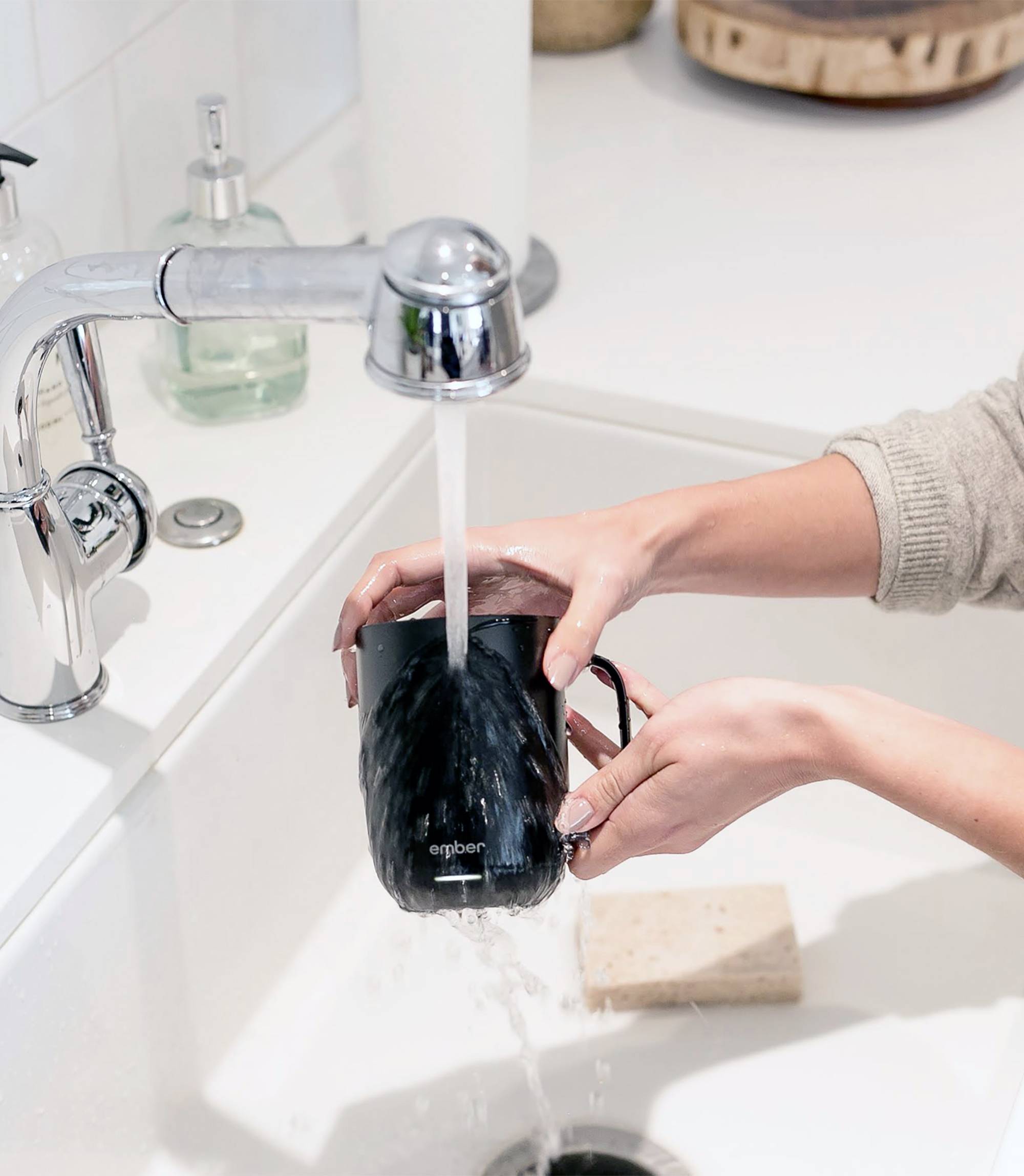 Eine Person spült eine schwarze Tasse unter fließendem Wasser in einer Küchenspüle ab. Im Hintergrund sind Seifenspender sichtbar.