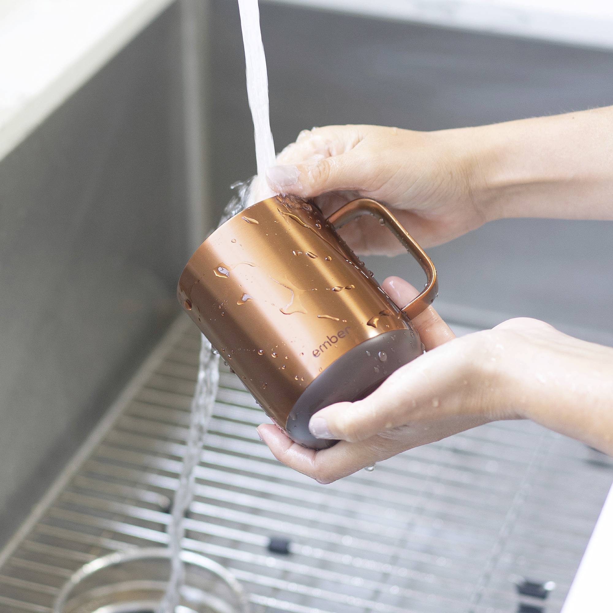 Eine Person wäscht eine kupferfarbene Tasse unter fließendem Wasser in einem Spülbecken.