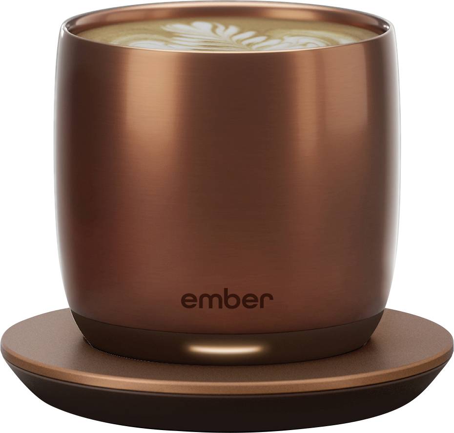 Eine kupferfarbene Tasse mit Latte Art auf einem Tisch. Die Tasse hat das Logo 'ember'.