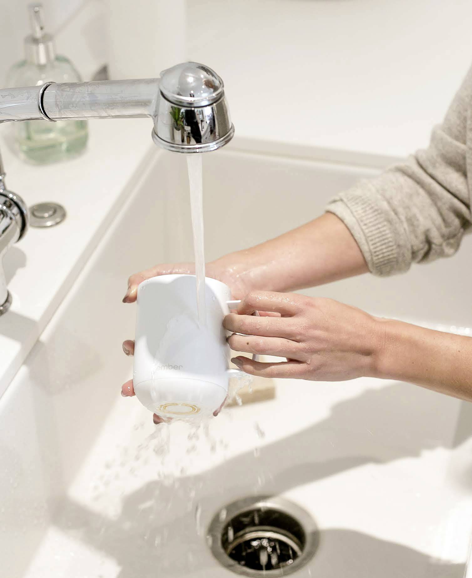 Eine Person spült eine weiße Tasse unter fließendem Wasser in einem Waschbecken ab. Die rechte Hand hält die Tasse, während die linke sie reinigt.