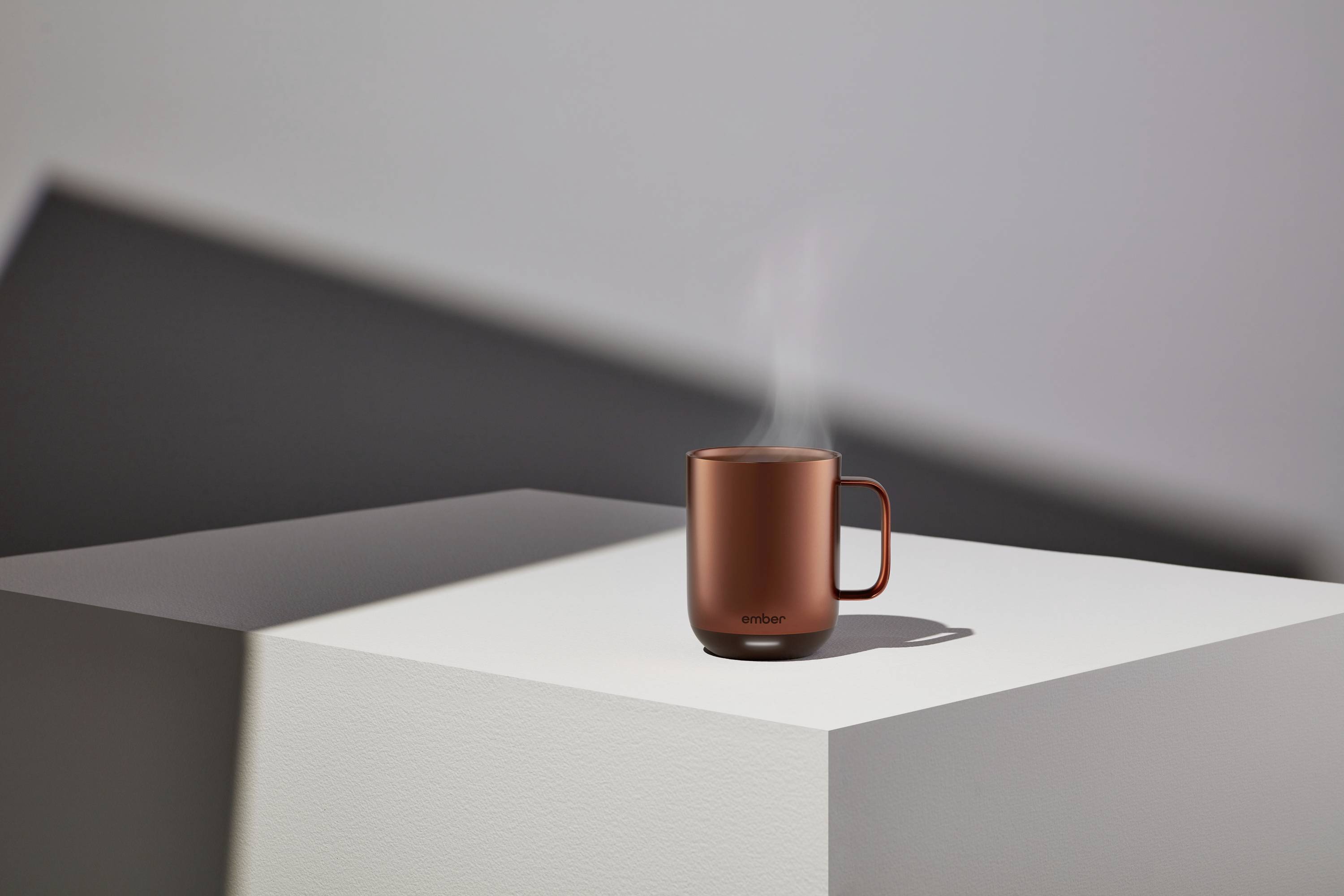 Eine rote Tasse mit dampfendem Getränk steht auf einem weißen Podest. Schattierungen im Hintergrund betonen die minimalistische Szene.