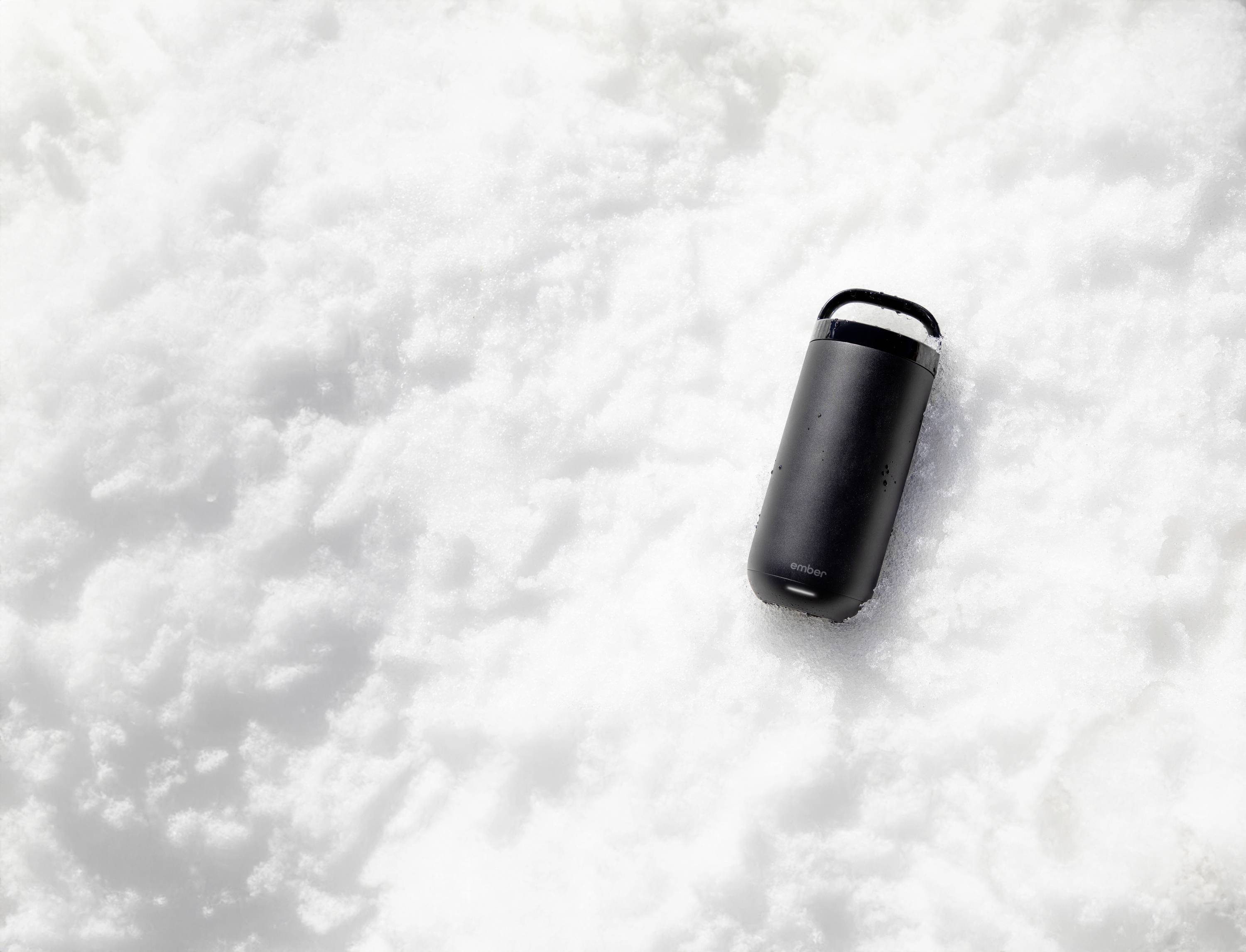 Ein schwarzer Kaffeebecher liegt im Schnee.