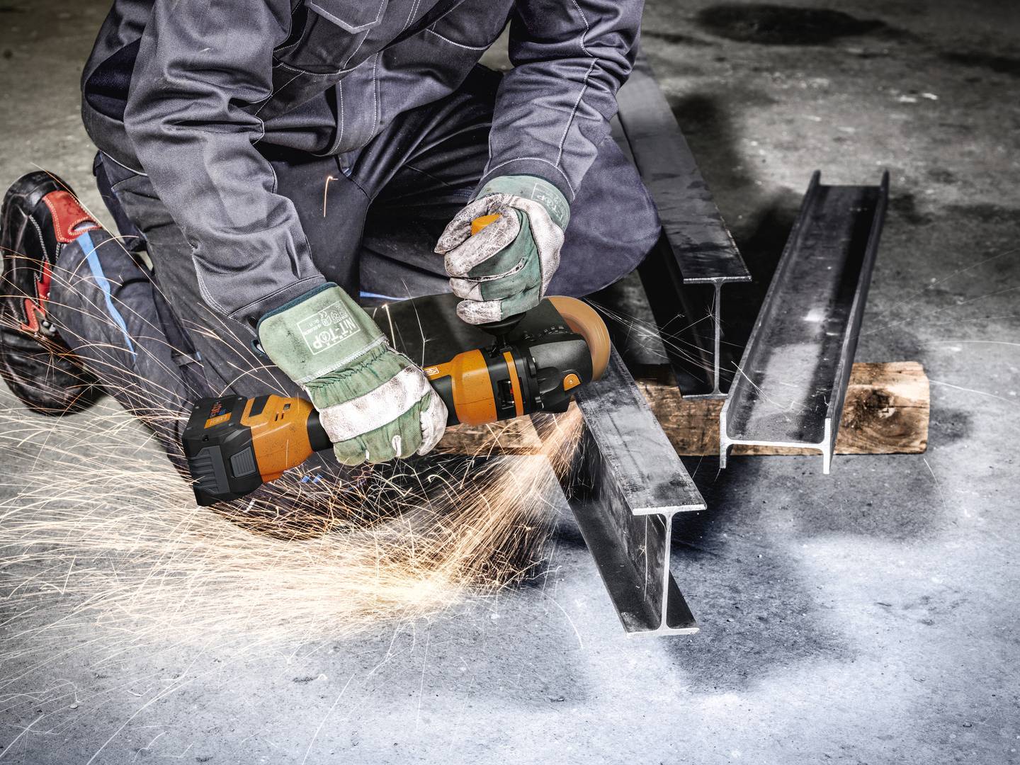 Person schneidet Metallträger mit Winkelschleifer, Funken sprühen. Schutzhandschuhe und Arbeitskleidung sind erkennbar.