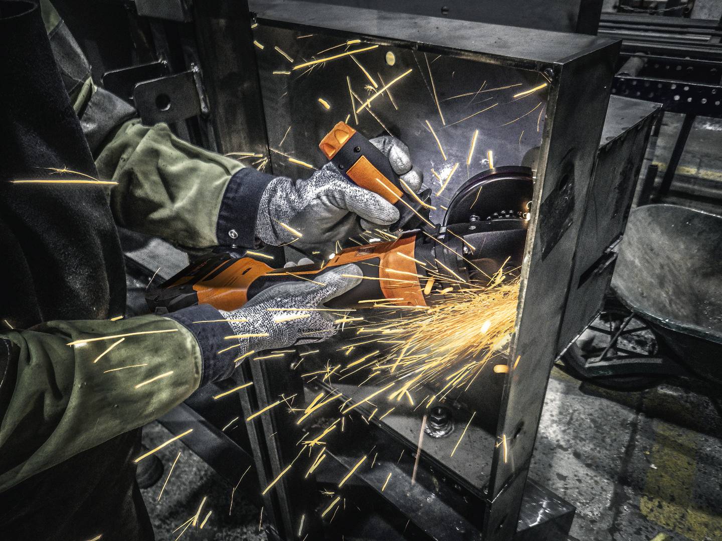 Ein Werker in Schutzkleidung erzeugt Funken, indem er mit einem Winkelschleifer Metall bearbeitet.