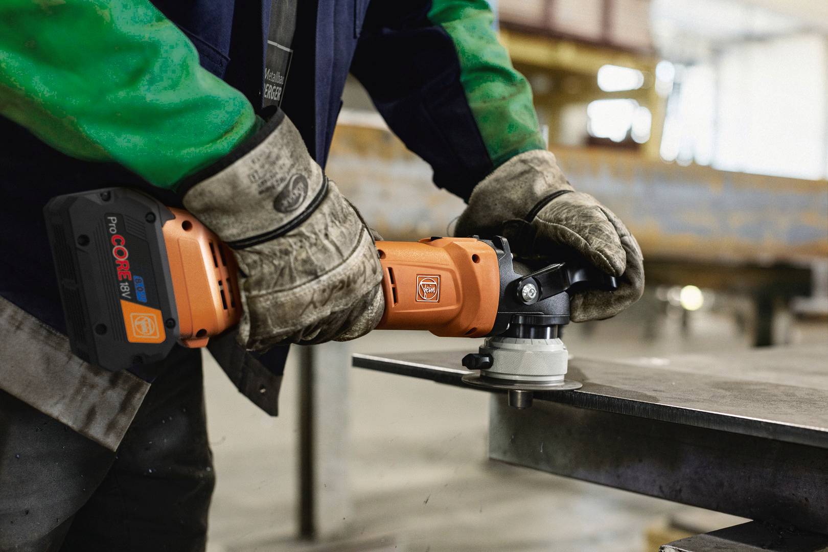 Eine Person in Arbeitskleidung schleift mit einer elektrischen Schleifmaschine Metall. Schutzkleidung und handwerkliche Tätigkeit sind erkennbar.