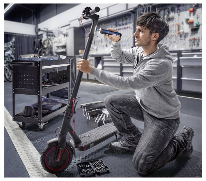 Eine Person repariert einen Elektroroller in einer Werkstatt. Sie hält ein Werkzeug in der Hand und arbeitet konzentriert am Lenker.