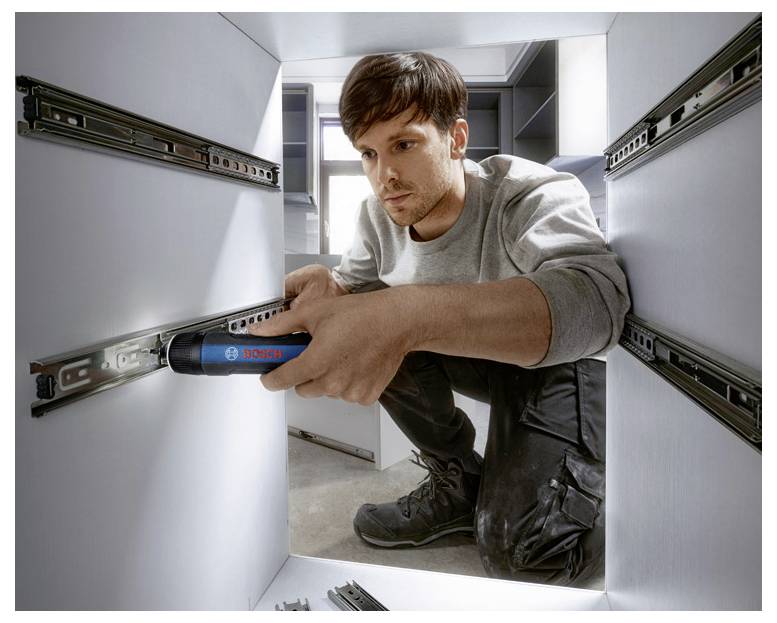 Ein Handwerker installiert eine Schubladenführung mit einem blauen Elektrowerkzeug in einer hellen, modernen Küche.