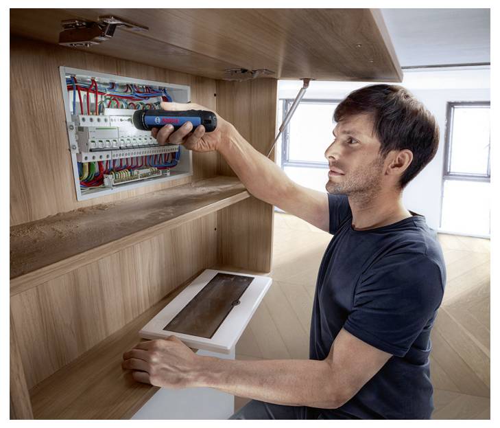 Ein Mann repariert einen Stromkasten mit einem elektrischen Schraubendreher in einem Holzschrank.