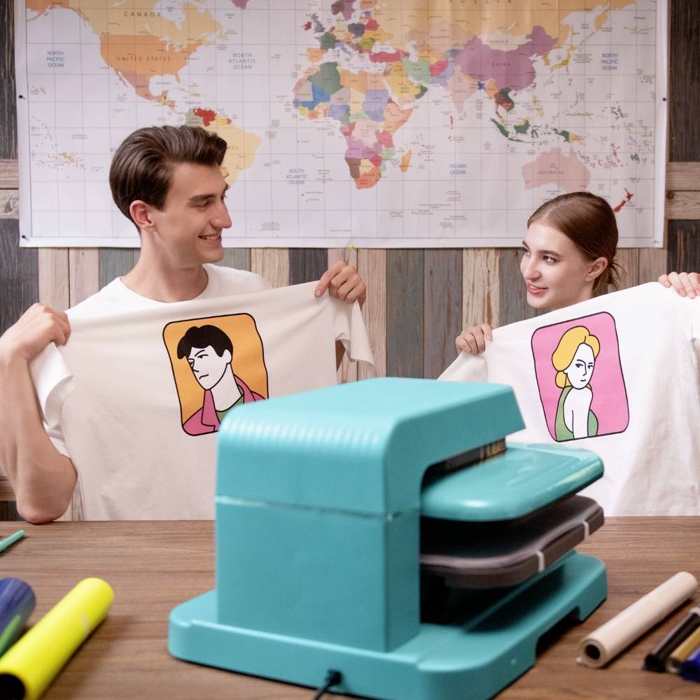 Ein Mann und eine Frau präsentieren bedruckte T-Shirts mit Illustrationen. Im Hintergrund hängt eine Weltkarte an der Wand.