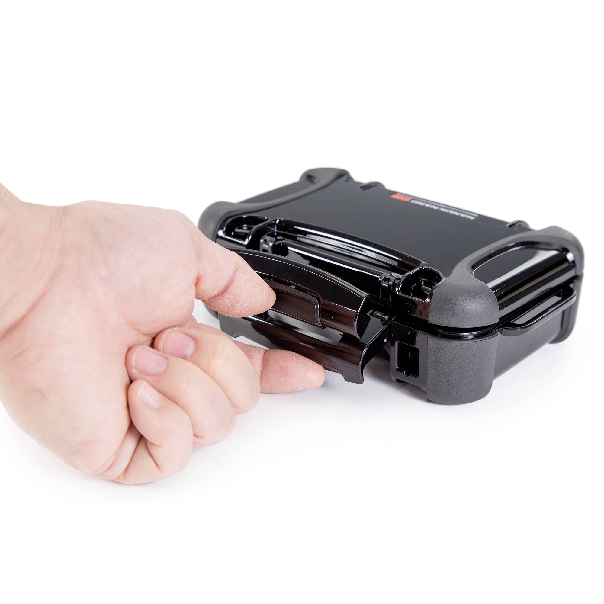 Eine Hand zeigt mit dem Daumen auf einen kleinen schwarzen Schutzkoffer mit Schnappverschluss. Der Koffer ist geschlossen.