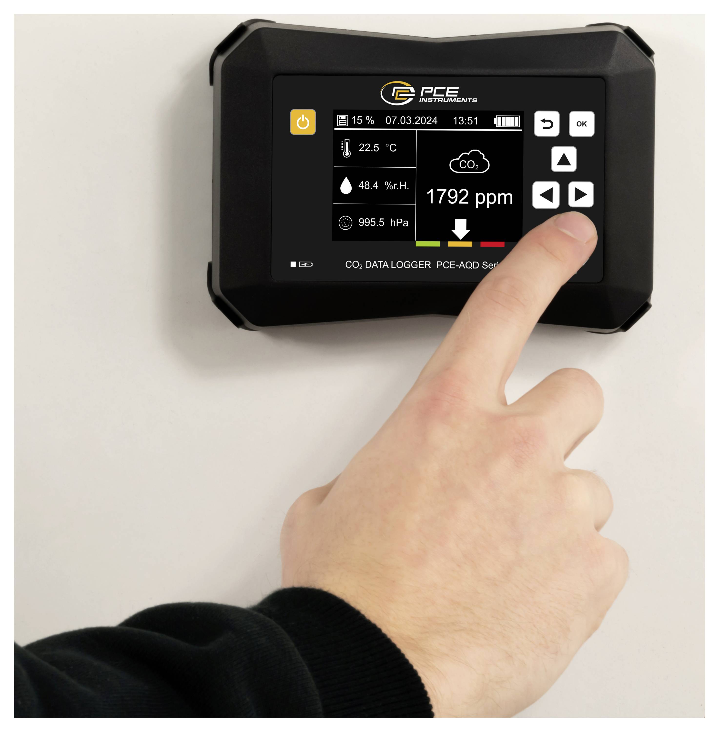 Hand drückt ein an der Wand montiertes CO2-Datenlogger-Gerät, das auf seinem Display 1792 ppm, 22,5°C, 48,4% Luftfeuchtigkeit und 995,5 hPa anzeigt.