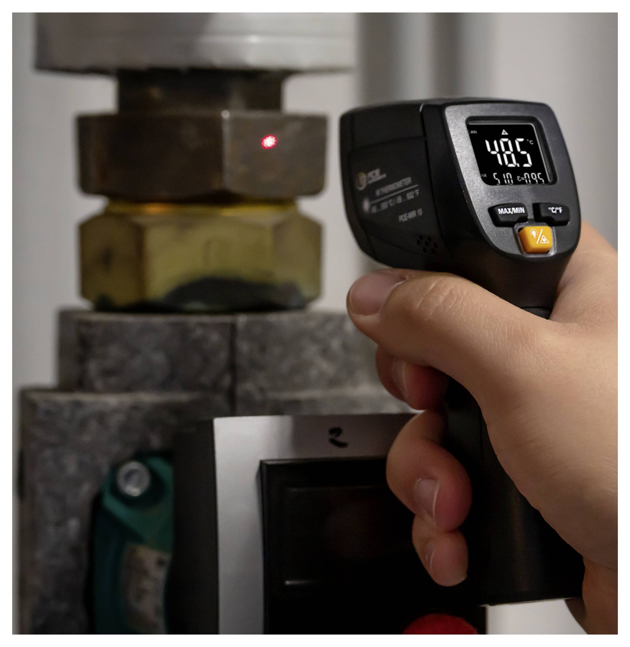 Eine Person zielt mit einem tragbaren Infrarot-Thermometer auf ein Maschinenteil, wobei das Thermometer eine Temperaturanzeige von 48,9°C zeigt.