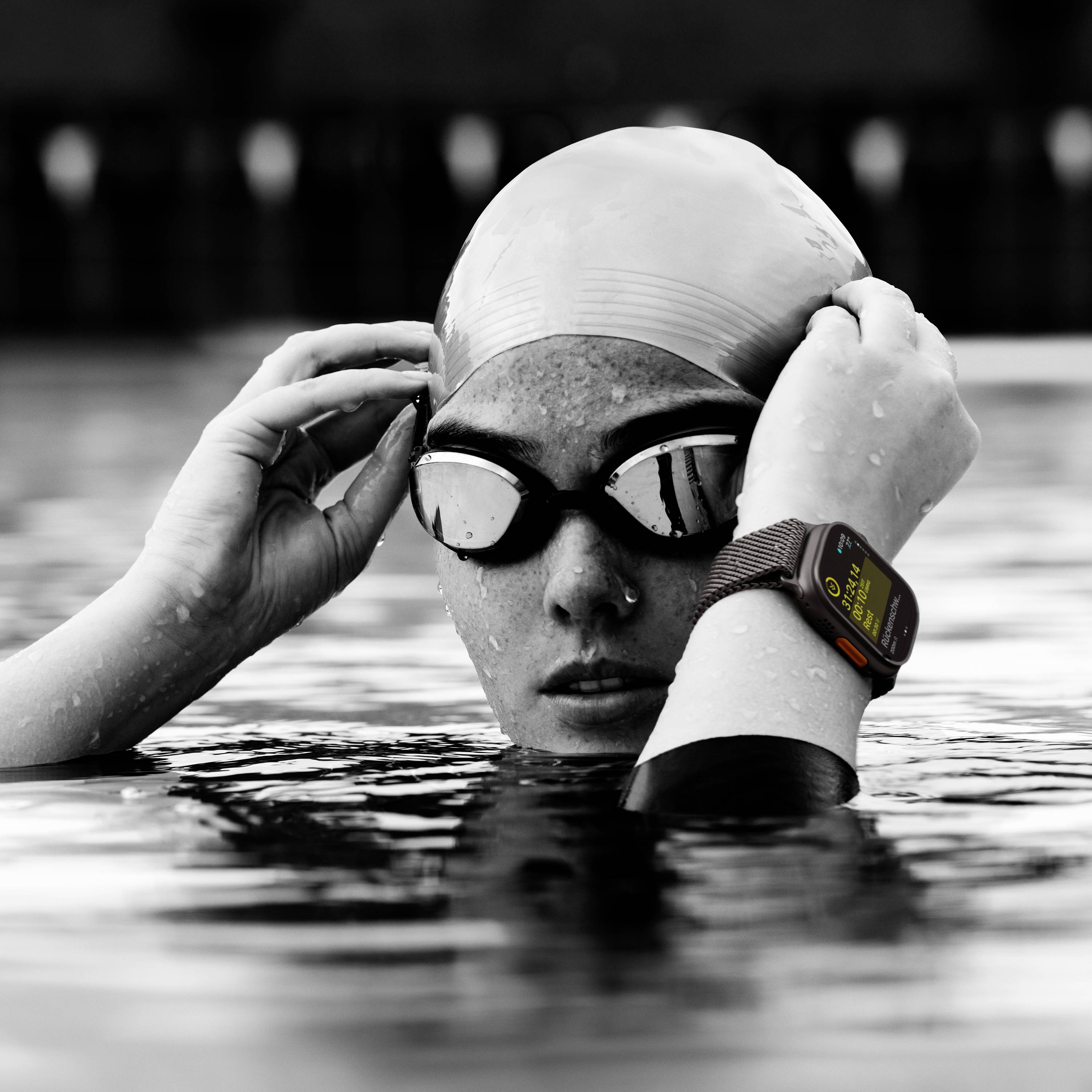 Eine Person im Schwimmbecken trägt eine Schwimmbrille und eine Schwimmkappe. Am Handgelenk ist eine Smartwatch zu sehen.