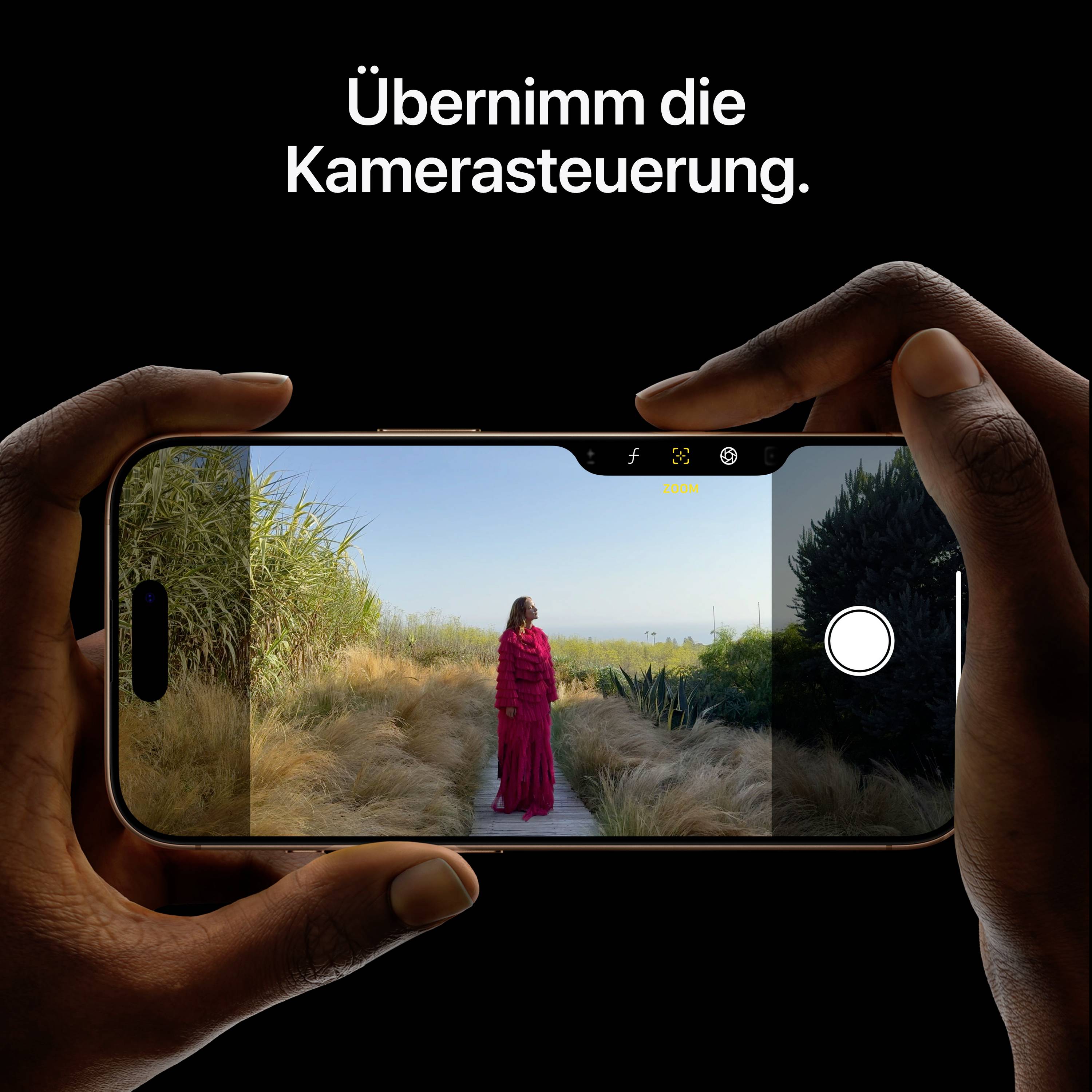 Zwei Hände halten ein Smartphone, das eine Frau in rotem Kleid in einer Wüstenlandschaft fotografiert. Text: 'Übernimm die Kamerasteuerung'.