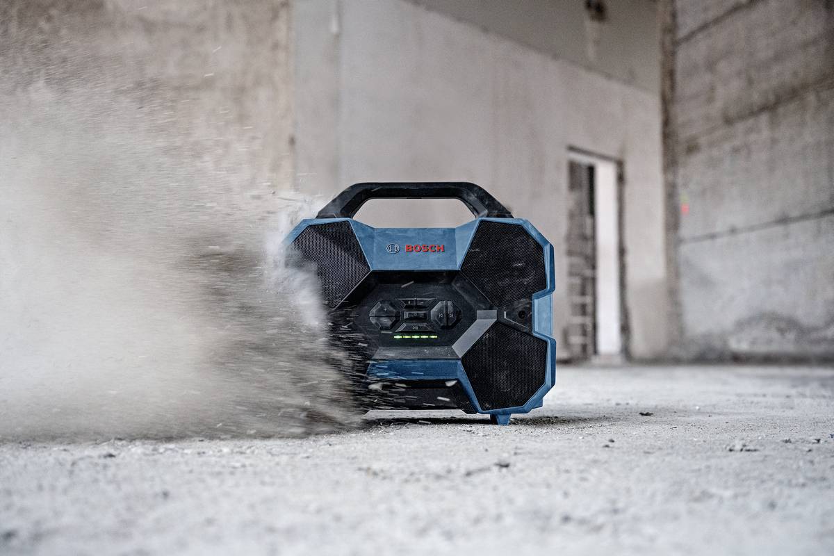Ein tragbares Radio auf einer Baustelle wirbelt Staub auf. Es hat ein robustes Design und ist an groben Oberflächen angepasst.