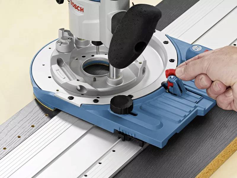 Oberfräse wird auf Holzbrett geführt. Eine Hand hält das Werkzeug, bereit zur Feineinstellung. Funktionseinstellung deutlich erkennbar.