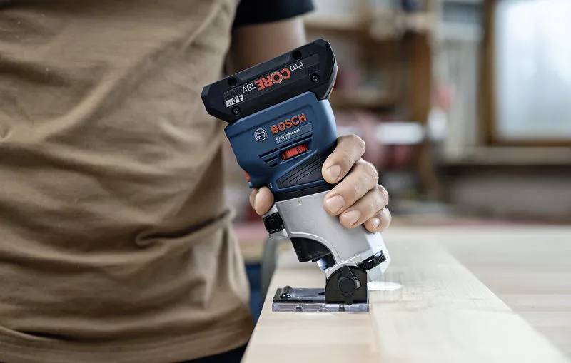 Eine Person setzt eine Bosch-Kantenschleifmaschine auf ein Holzbrett an; der Fokus liegt auf der präzisen Holzbearbeitung.