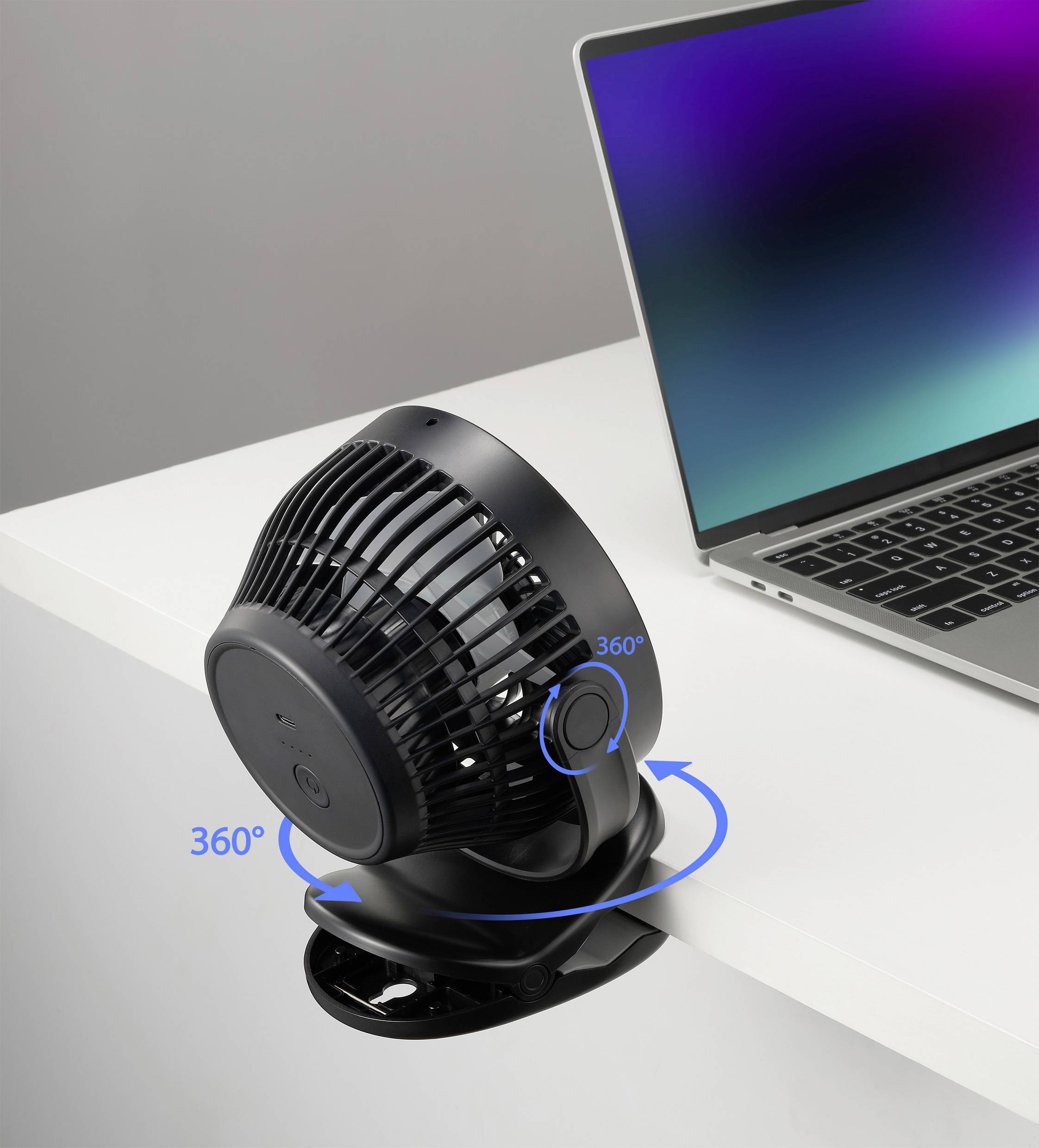 Ein schwarzer, runder Ventilator ist an der Tischkante befestigt und kann sich um 360 Grad drehen. Daneben steht ein Laptop.