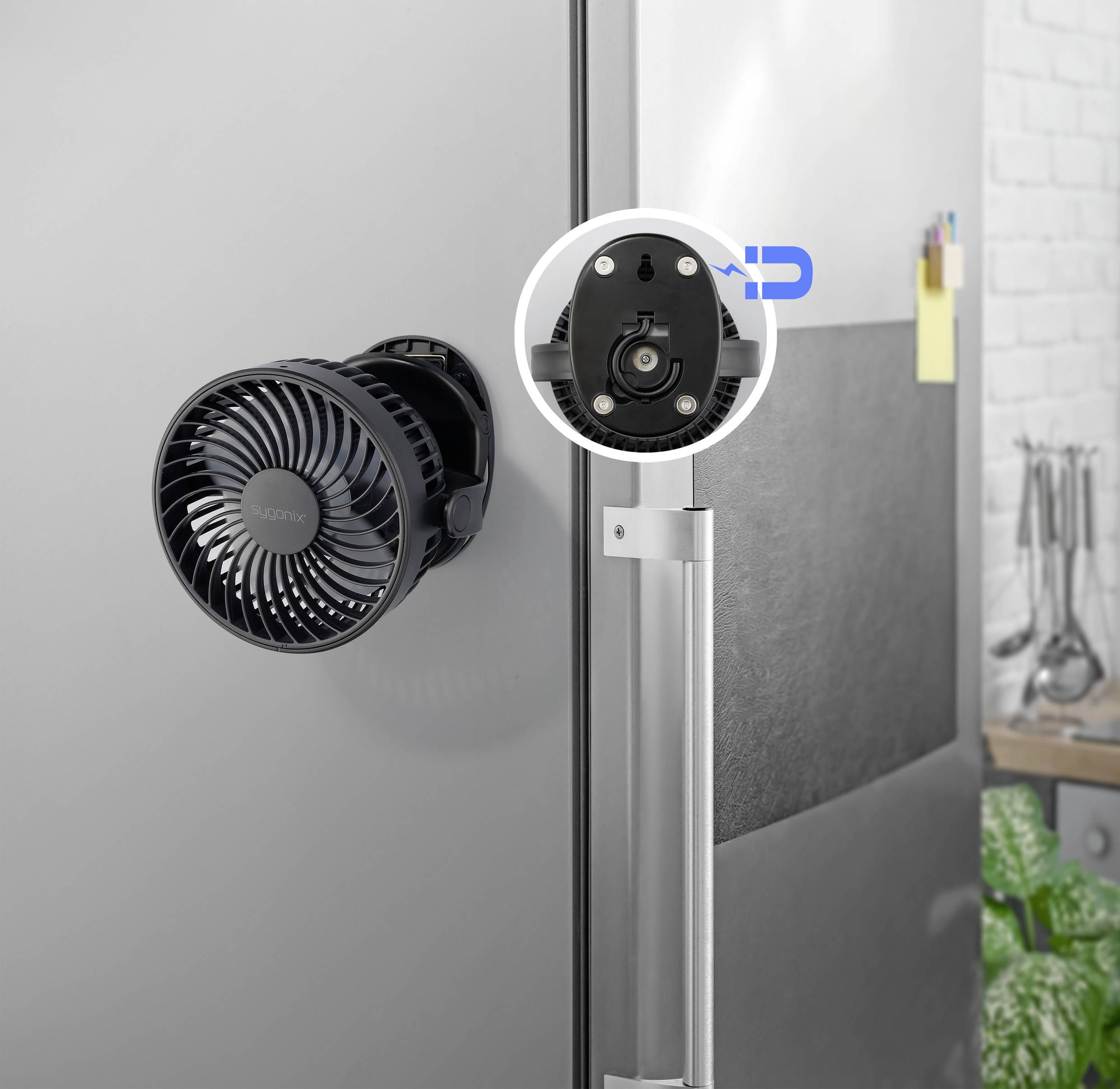 Ein schwarzer Ventilator ist mithilfe eines Magneten an einer Kühlschranktür befestigt. In der Küche befinden sich Utensilien im Hintergrund.
