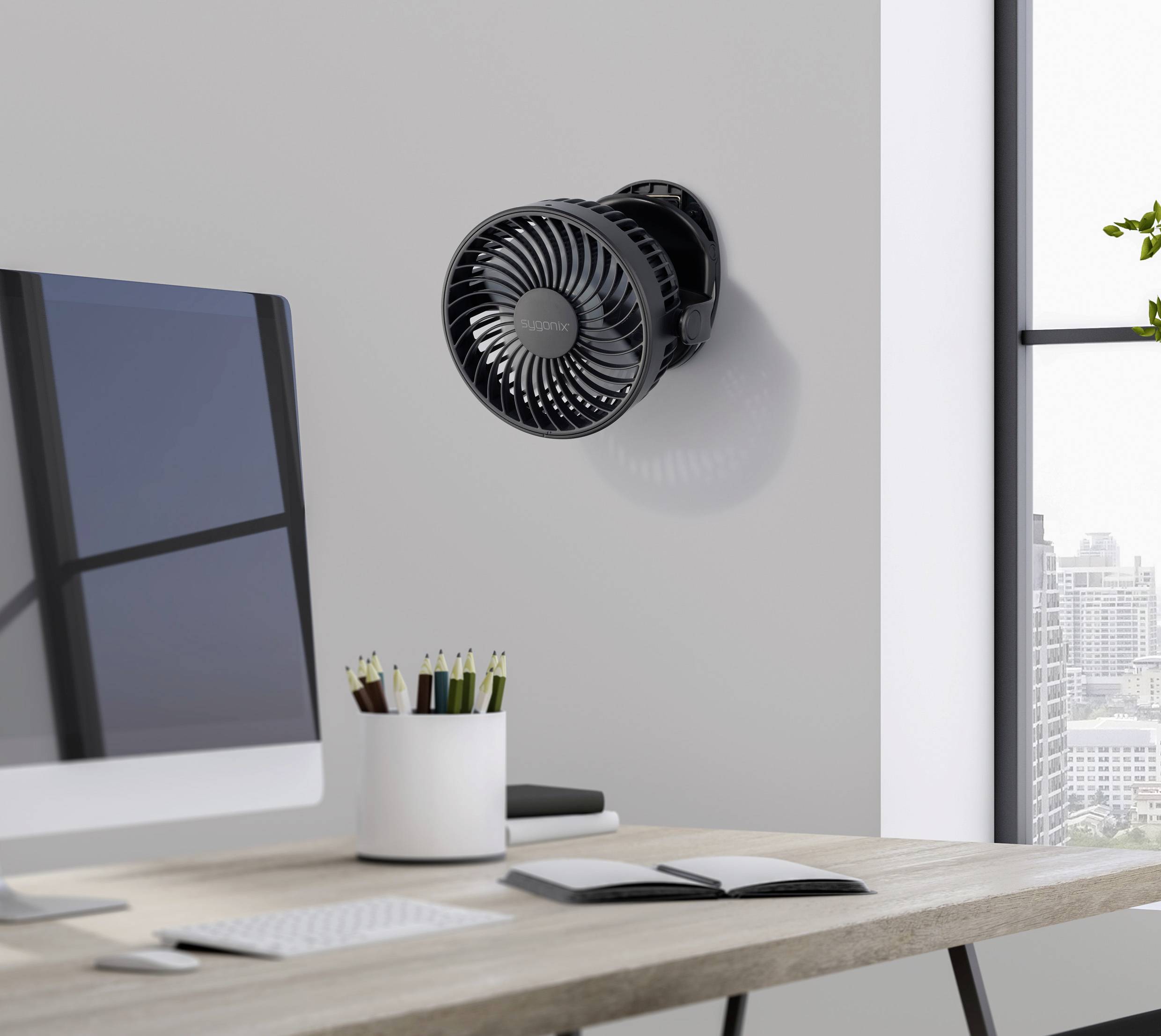 Ein schwarzer Ventilator ist an der Wand eines modernen Büros montiert. Der Raum hat einen Schreibtisch mit Schreibutensilien und ein Fenster mit Stadtblick.