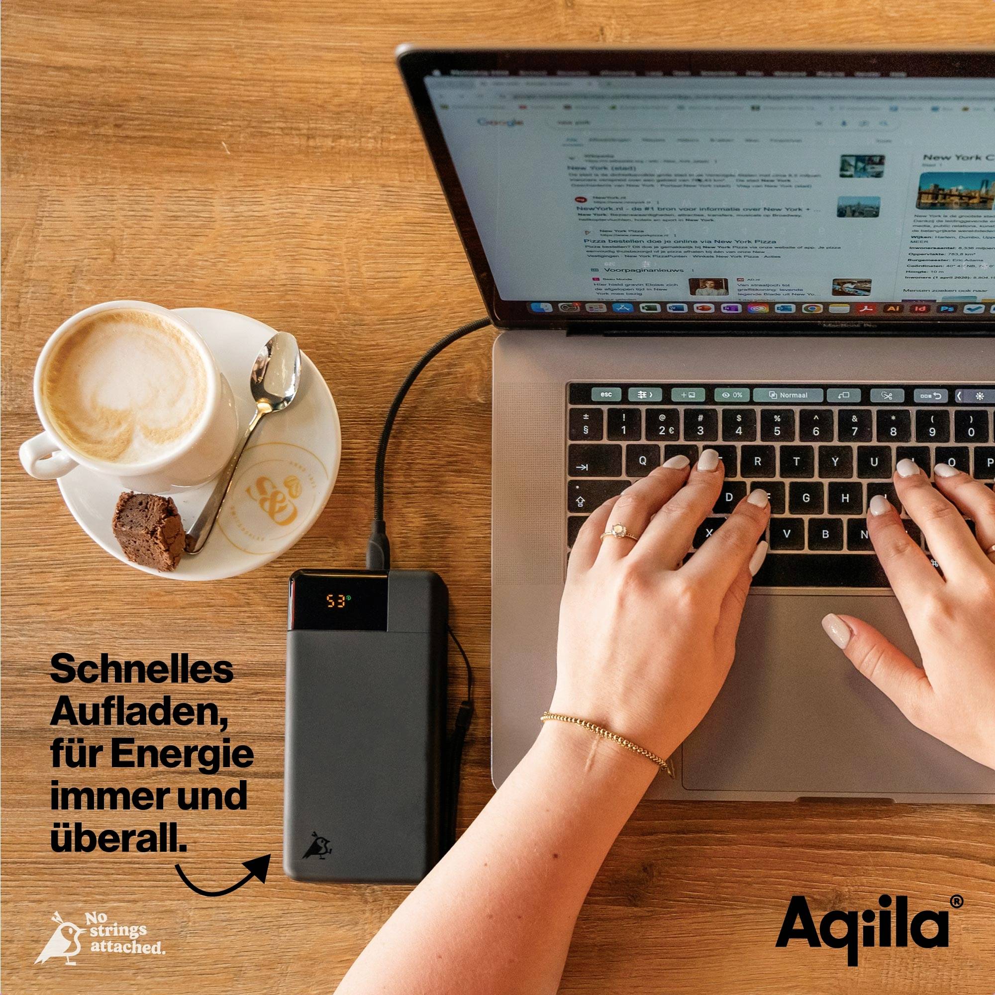 Eine Person arbeitet an einem Laptop, angeschlossen an eine Powerbank. Daneben stehen eine Tasse Kaffee und Kekse auf dem Tisch. Text im Bild: 'Schnelles Aufladen, überall.'
