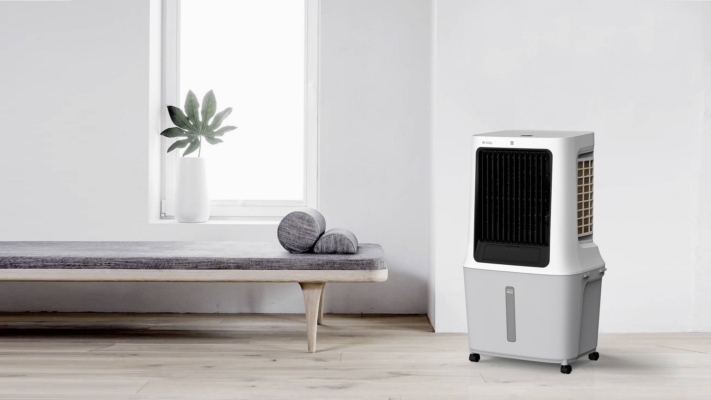 Ein Luftkühler steht in einem modernen, minimalistisch eingerichteten Raum mit Holzboden. Neben dem Kühler sind graue Kissen auf einer Bank.