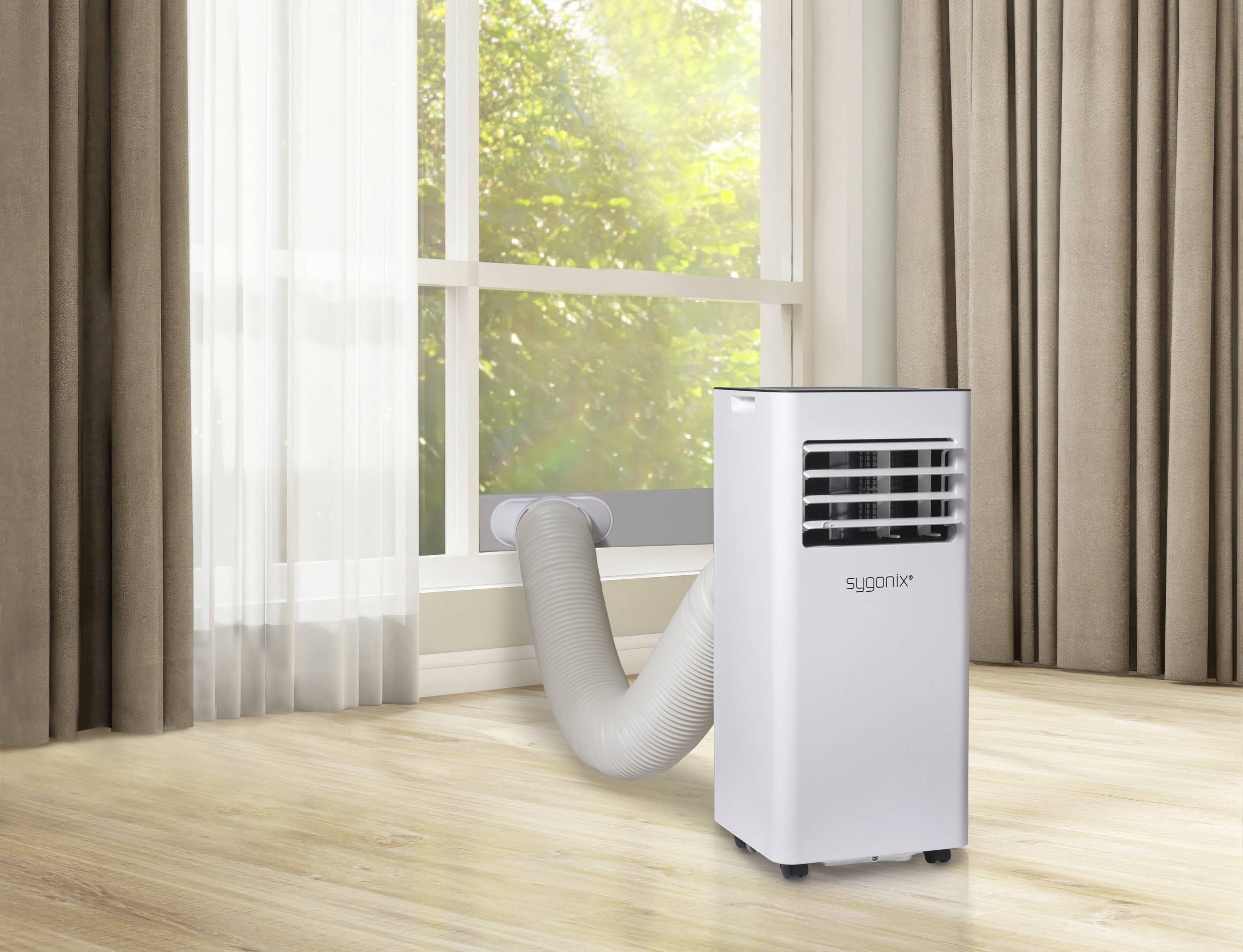 Mobiles Klimagerät in einem Raum, mit einem Abluftschlauch, der durch ein Fenster führt. Sonnenlicht scheint durch das Fenster.