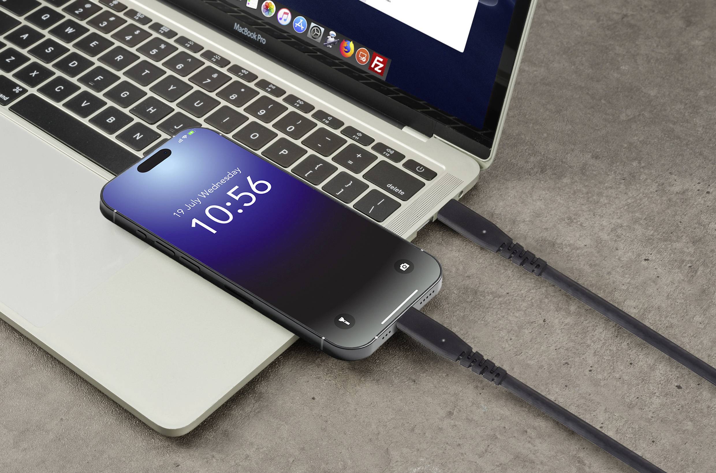 Ein Smartphone liegt auf einem Laptop und wird über ein USB-Kabel aufgeladen. Der Bildschirm zeigt Uhrzeit und Datum an.
