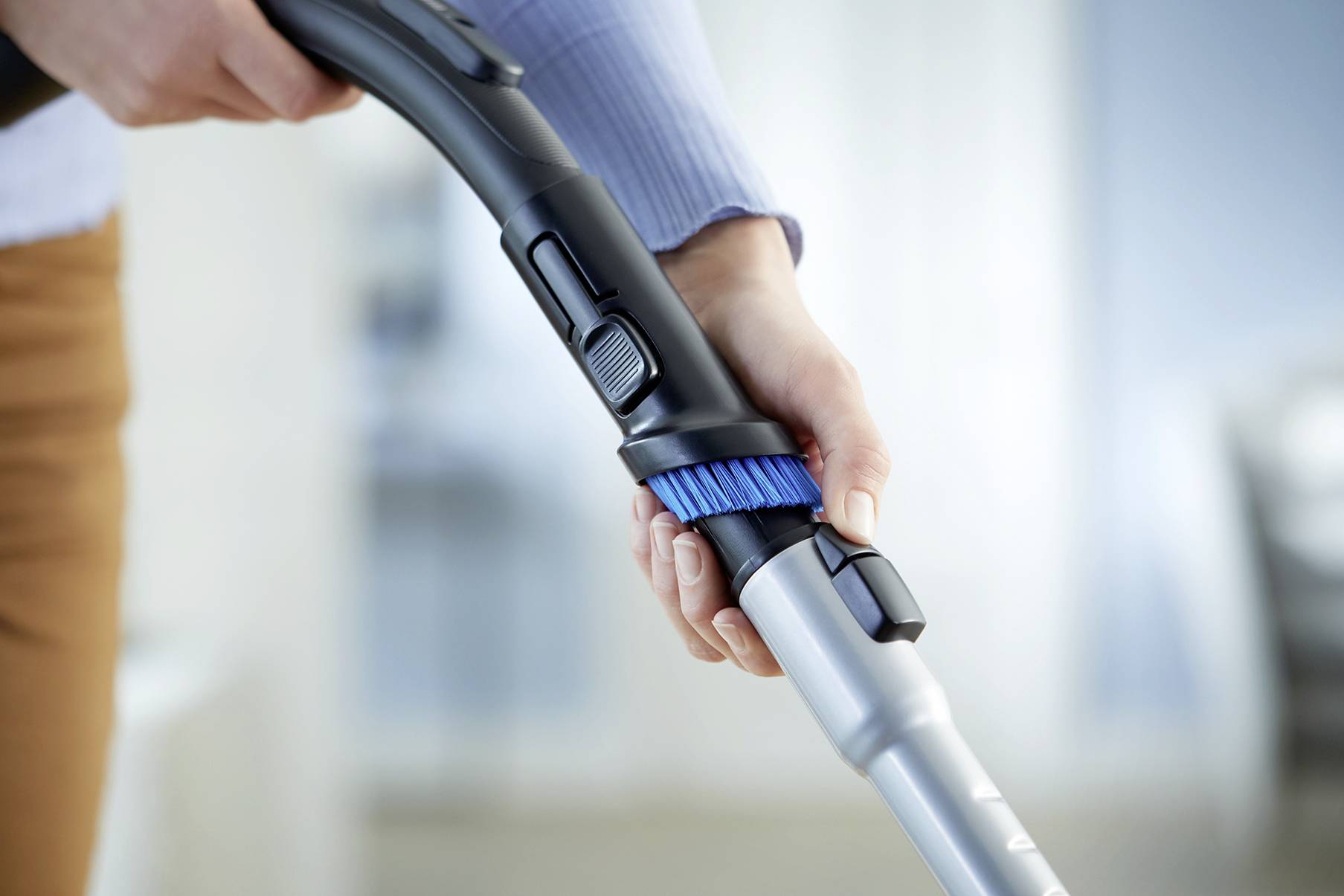 Person hält ein Staubsaugerrohr mit einer blauen Bürste, bereit zum Reinigen einer Oberfläche.