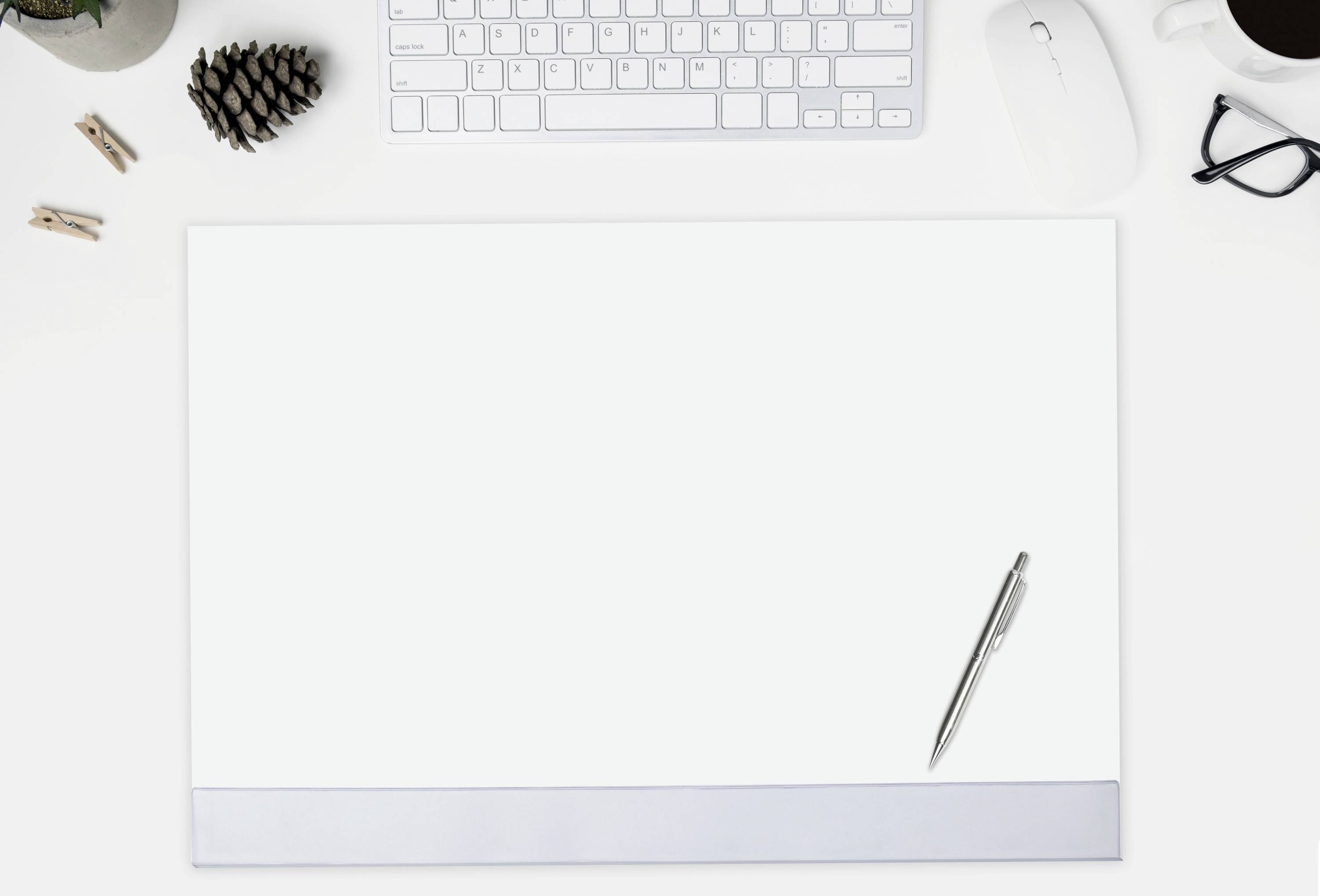 Ein Schreibtisch mit einer Computertastatur, Maus, Brille, Kaffeetasse und einem leeren Blatt Papier, auf dem ein Stift liegt.