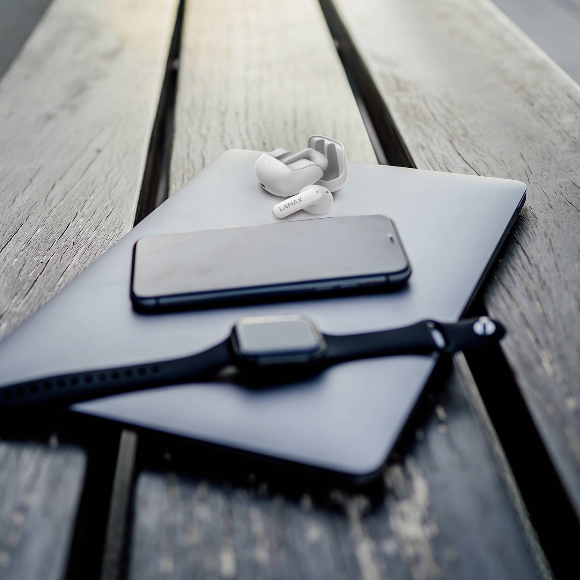 Smartwatch, Smartphone und kabellose Kopfhörer liegen auf einem Laptop auf einer Holzbank. Entspannte Technologiekonstellation.