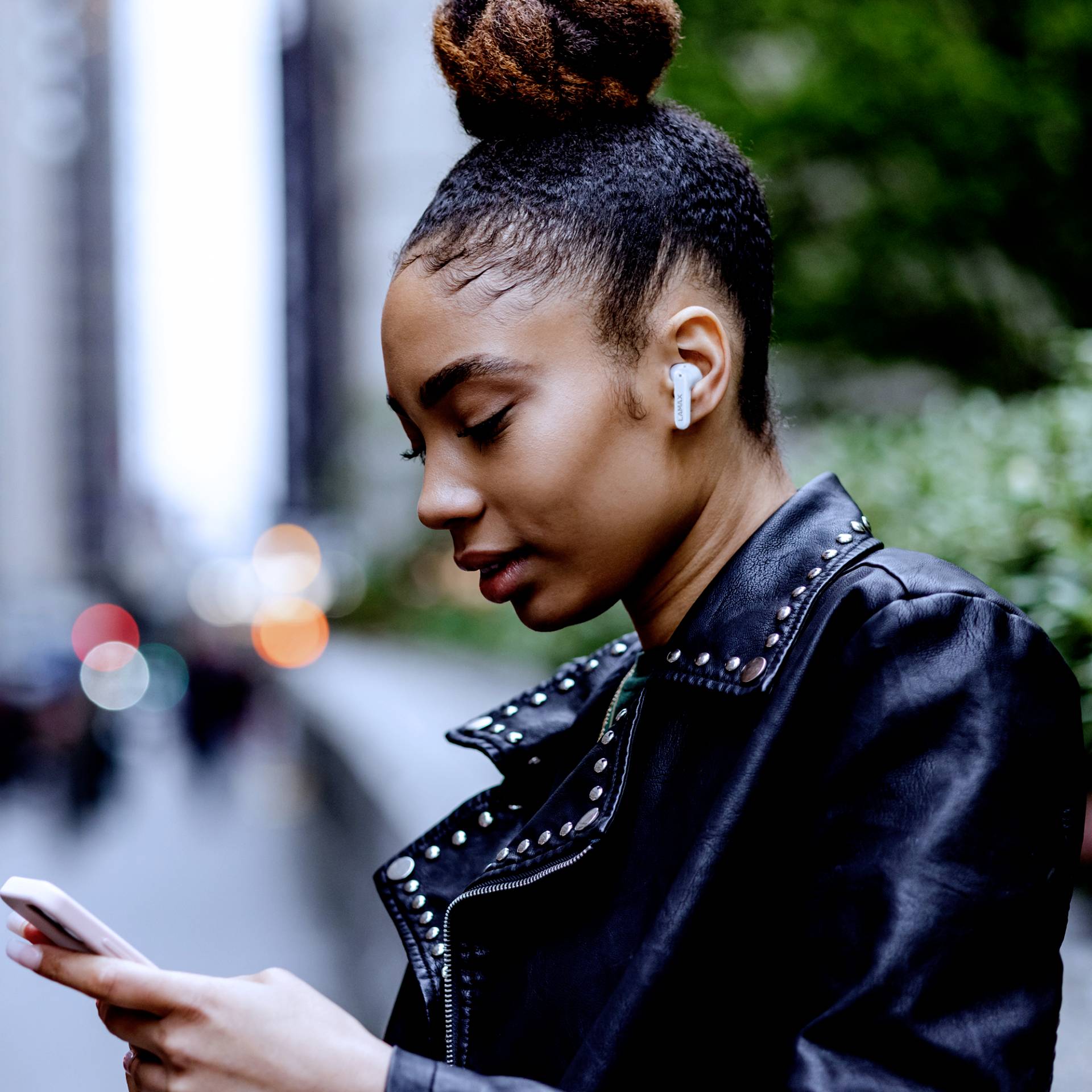Eine Person mit drahtlosen Ohrhörern geht in einer städtischen Umgebung und schaut auf ihr Smartphone.