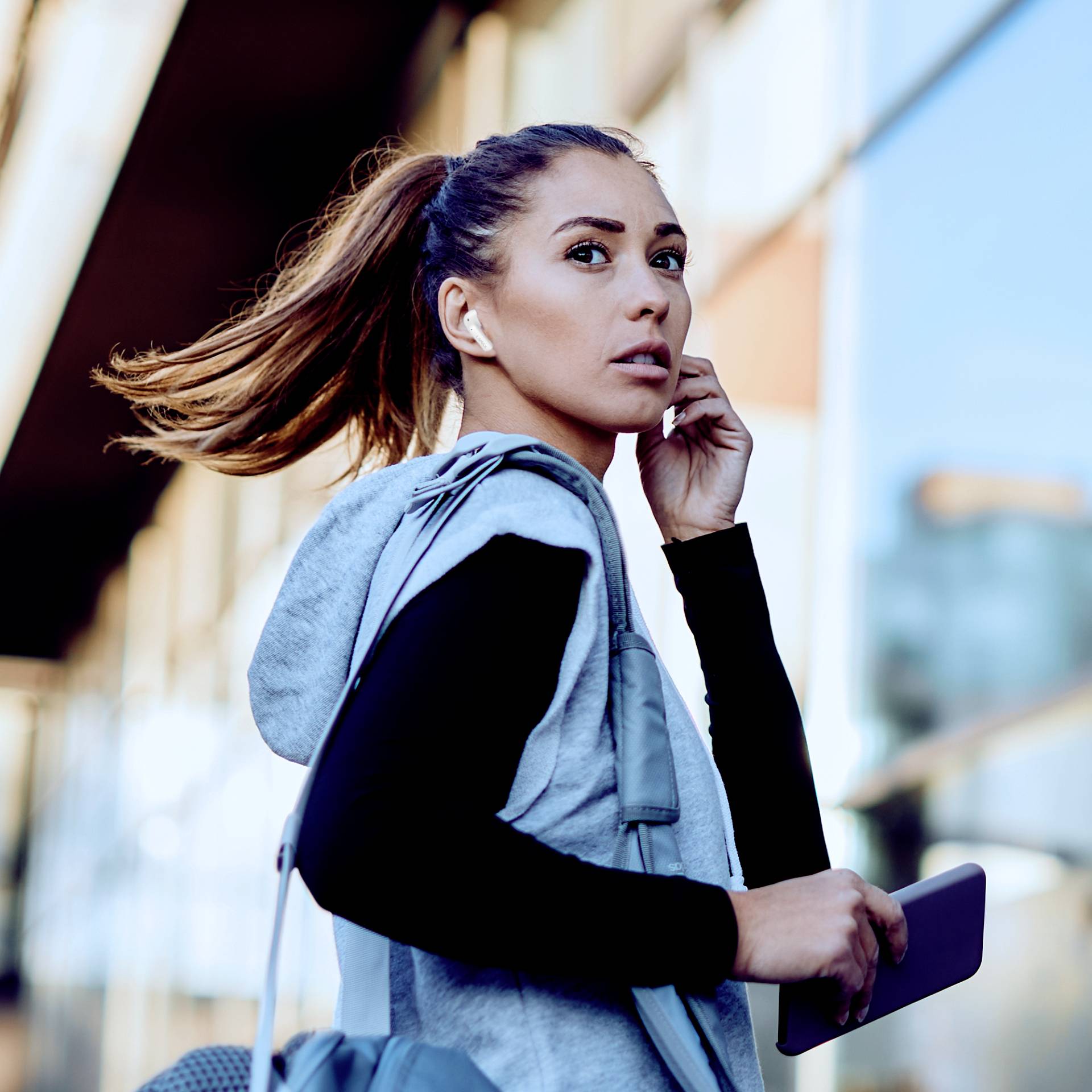 Eine Frau in Sportkleidung hält ein Smartphone in der Hand und blickt nachdenklich zur Seite, während sie draußen läuft.