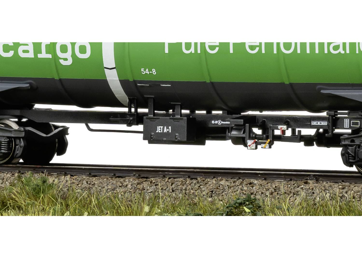 Ein grüner Zugwaggon mit der Aufschrift 'JET-A1' auf einem schwarzen Kasten an der Unterseite, fährt auf Schienen über eine grasbewachsene Fläche.