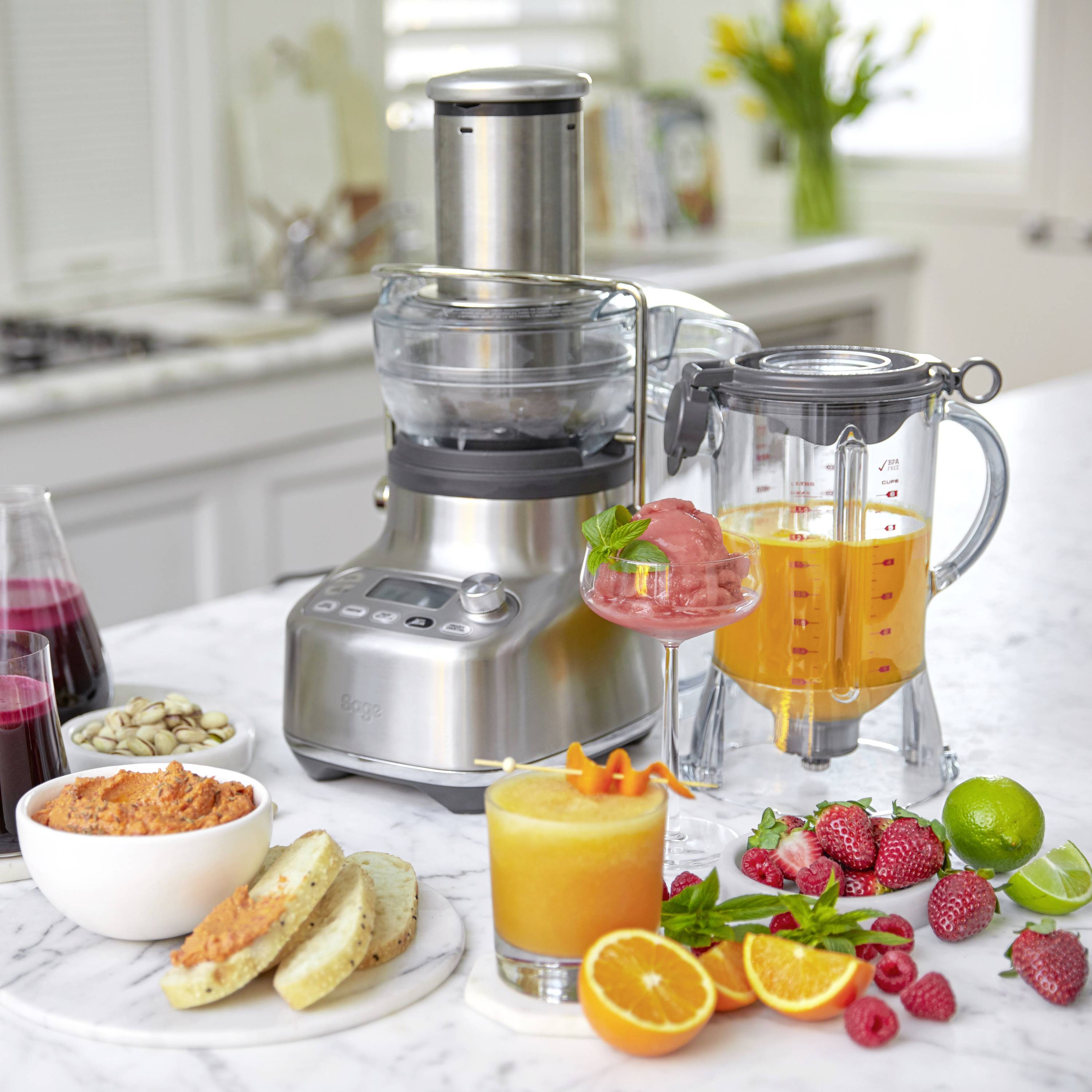 Küchenarbeitsplatte mit einem Entsafter, gefüllt mit Orangensaft, umgeben von frischen Früchten und ingeschenktem Saft.