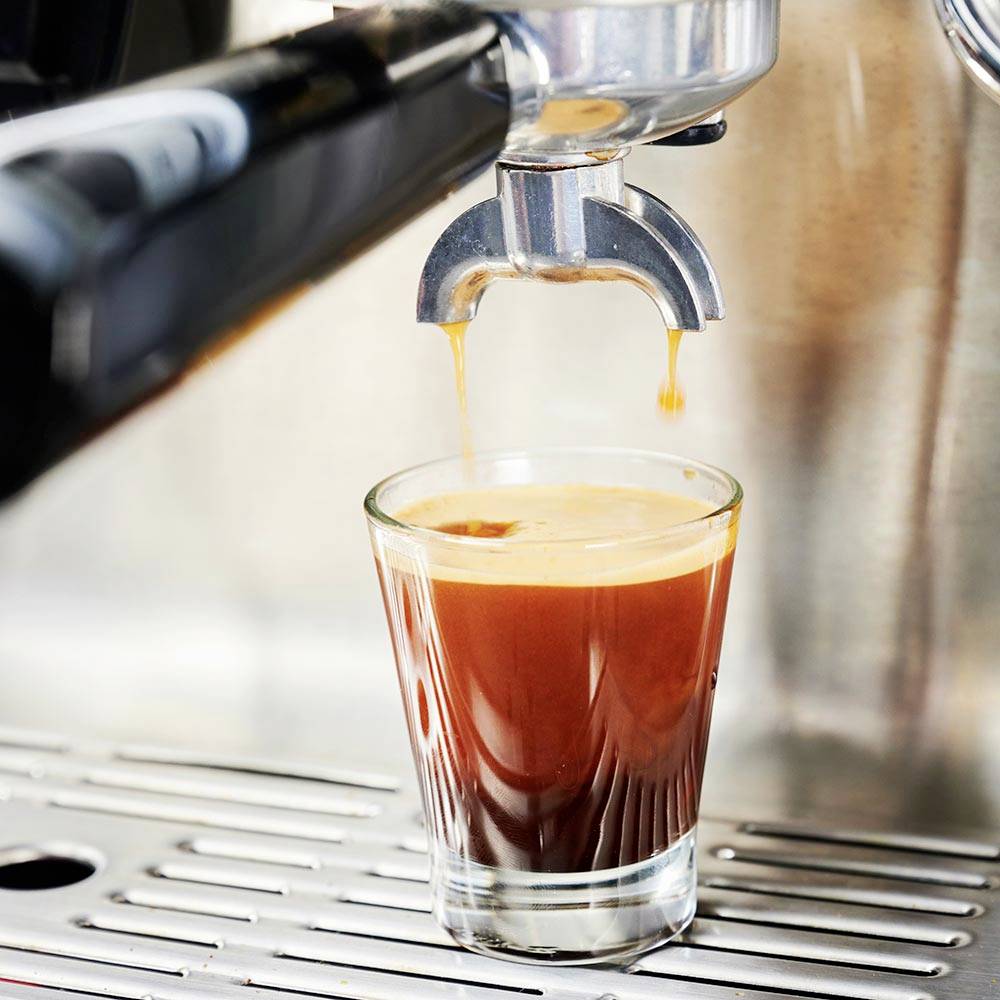 Espressomaschine füllt Glas mit frischem Espresso.