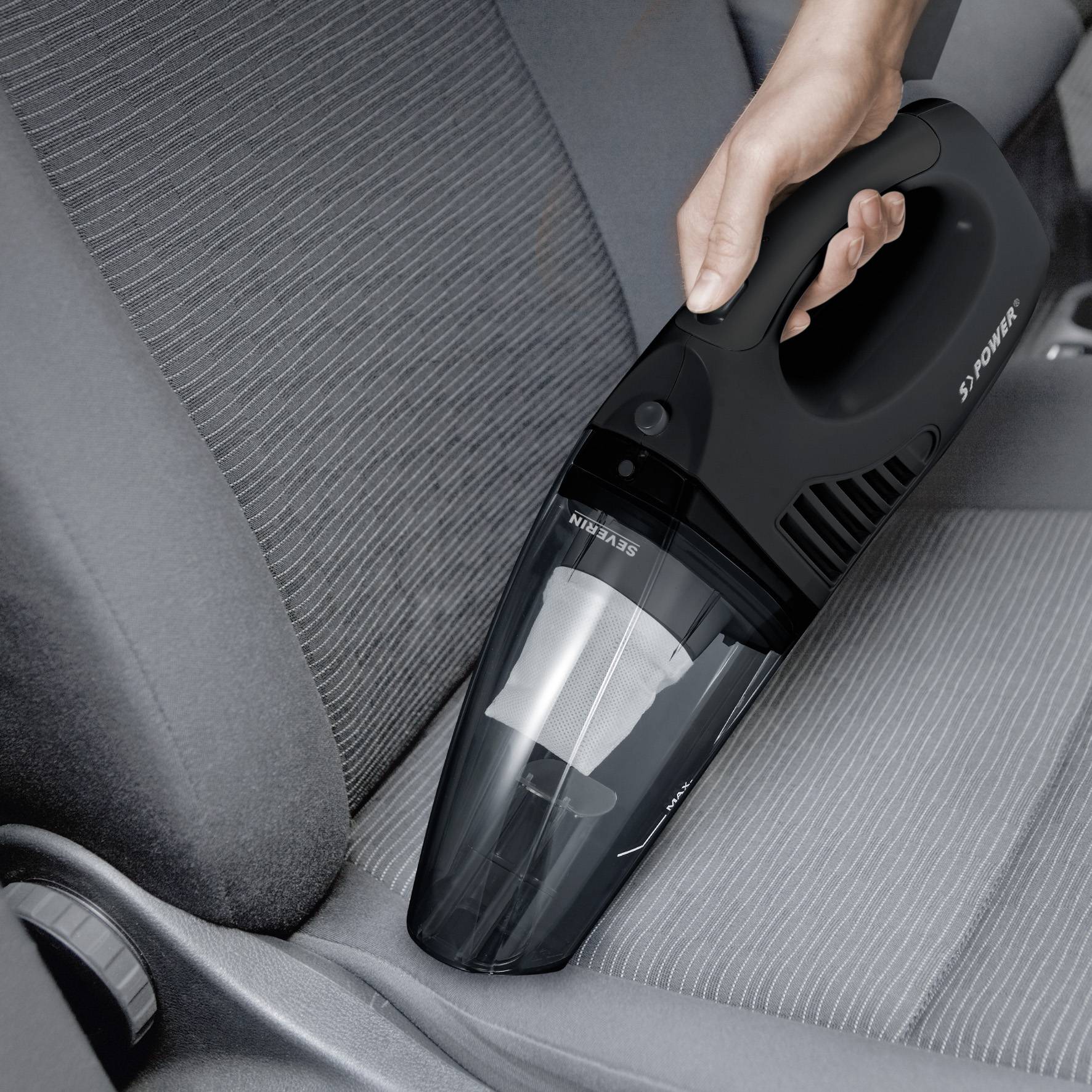 Eine Hand benutzt einen tragbaren Staubsauger, um den Sitz eines Autos zu reinigen. Der Staubsauger ist schwarz und handlich.
