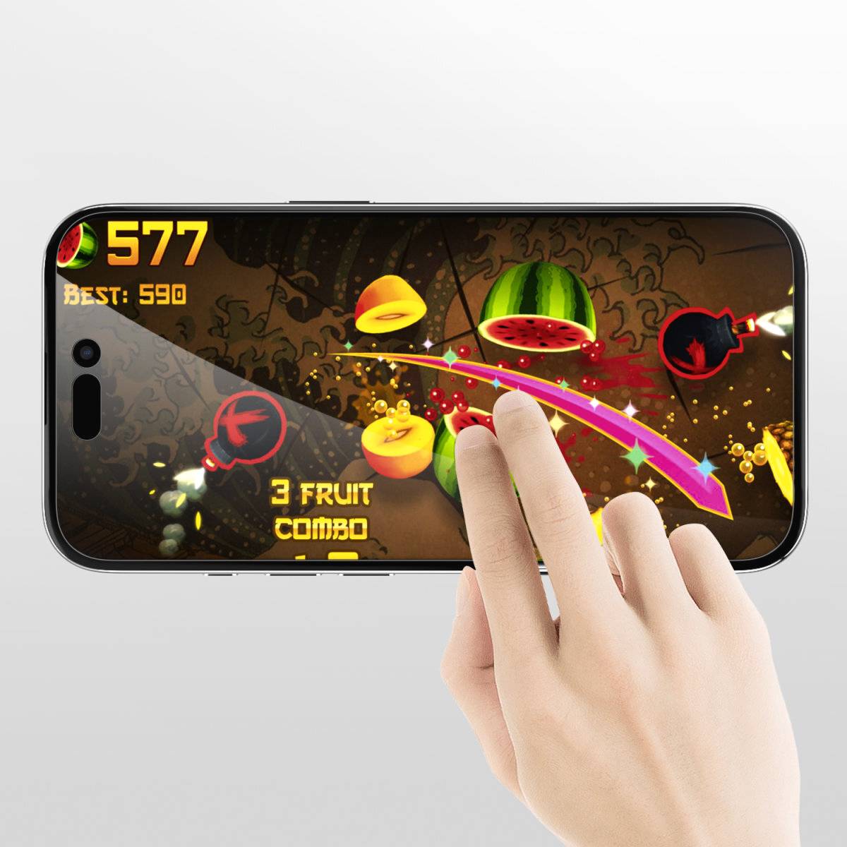 Eine Hand spielt ein Handyspiel, bei dem Obst mit Wischbewegungen zerschnitten wird. Punktestand zeigt 577 mit einem besten Ergebnis von 590.