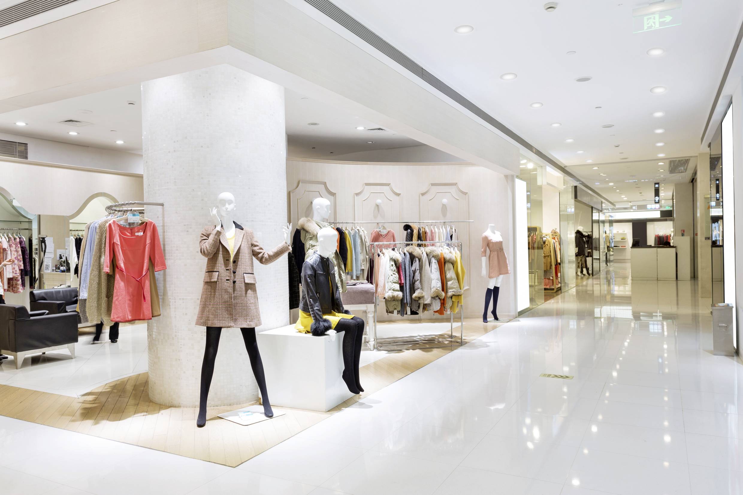 Ein modernes Bekleidungsgeschäft mit Schaufensterpuppen, die verschiedene Kleidung tragen. Im Hintergrund sind Regale mit weiteren Kleidungsstücken sichtbar.