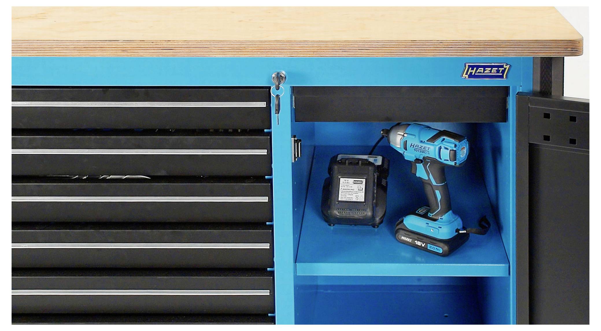 Blauer Werkzeugschrank mit halb geöffneter Tür und Schubladen. Darin steht ein blauer Akkuschrauber mit Ladegerät auf einem Regal.