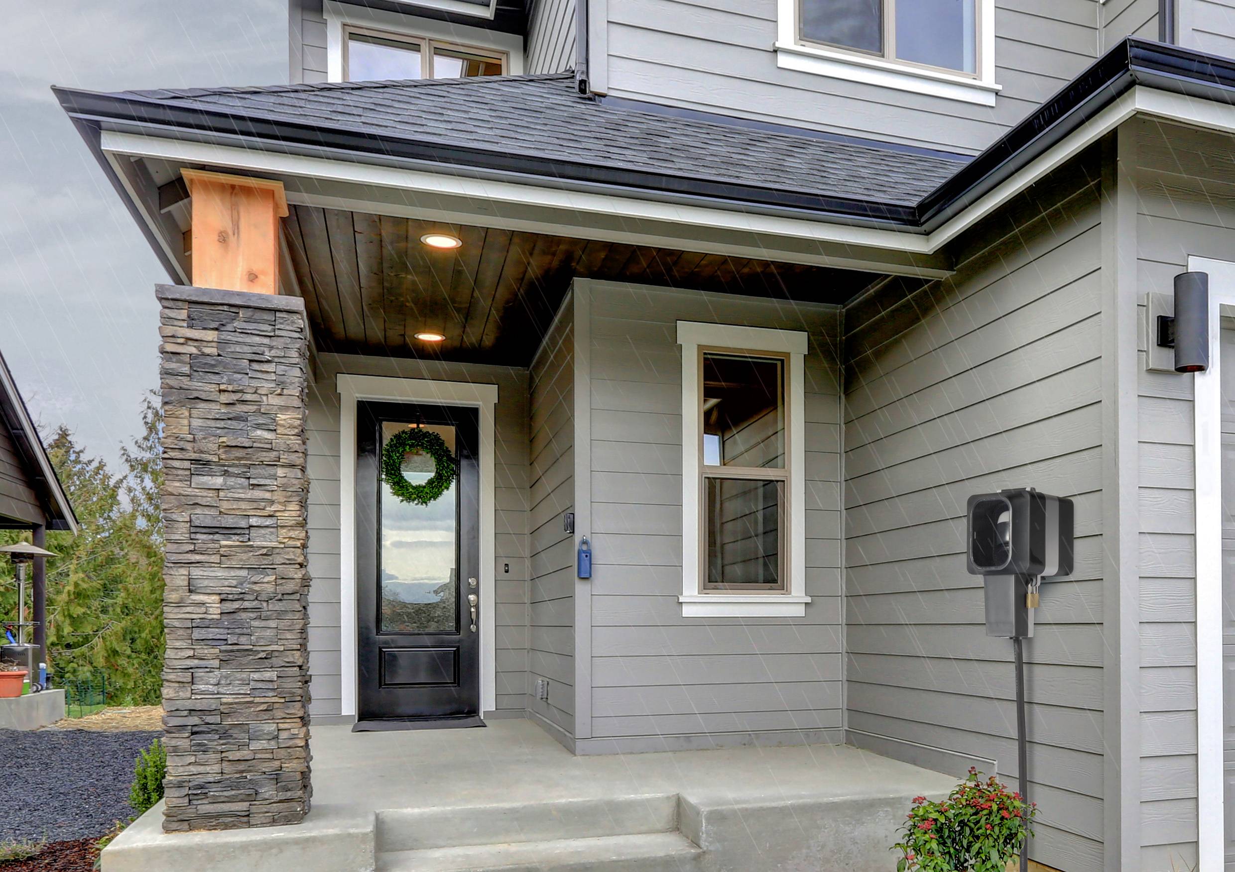 Eingang eines modernen Hauses mit grauer Holzfassade. Eine Kranzdekoration hängt an der schwarzen Eingangstür, rechts eine Ladestation.