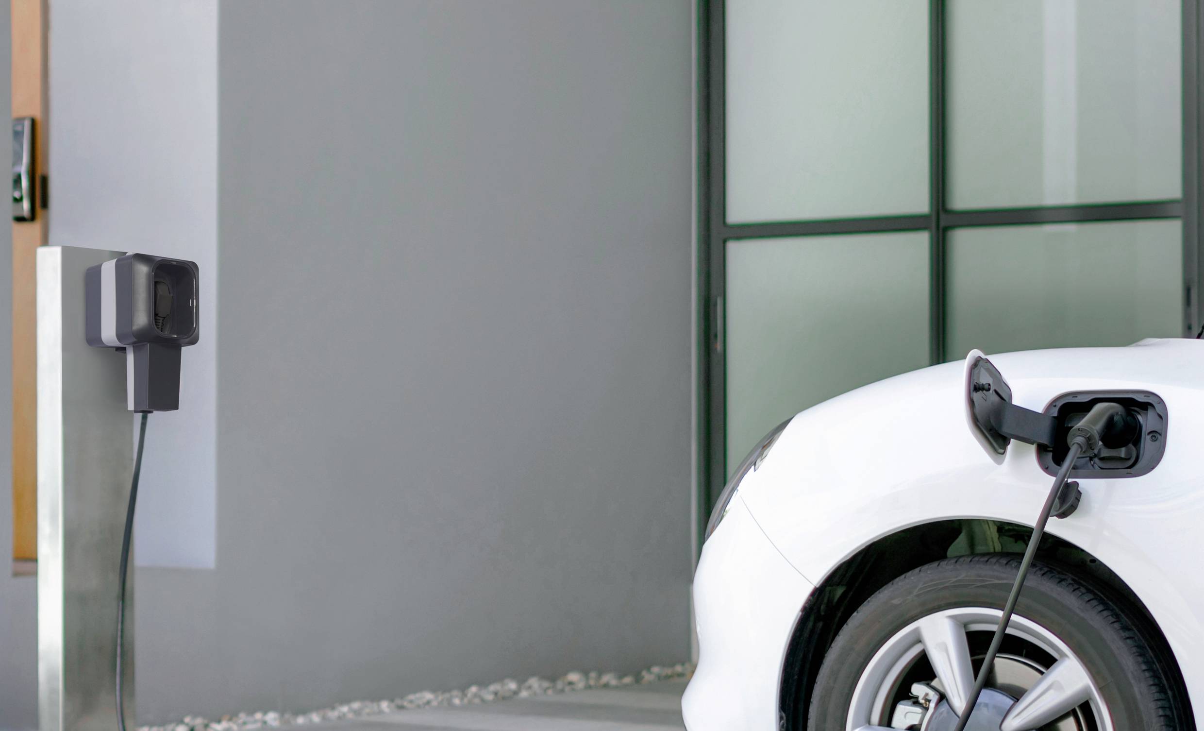 Ein weißes Elektroauto wird an einer Ladestation aufgeladen. Das Fahrzeug ist vor einem modernen Gebäude geparkt.