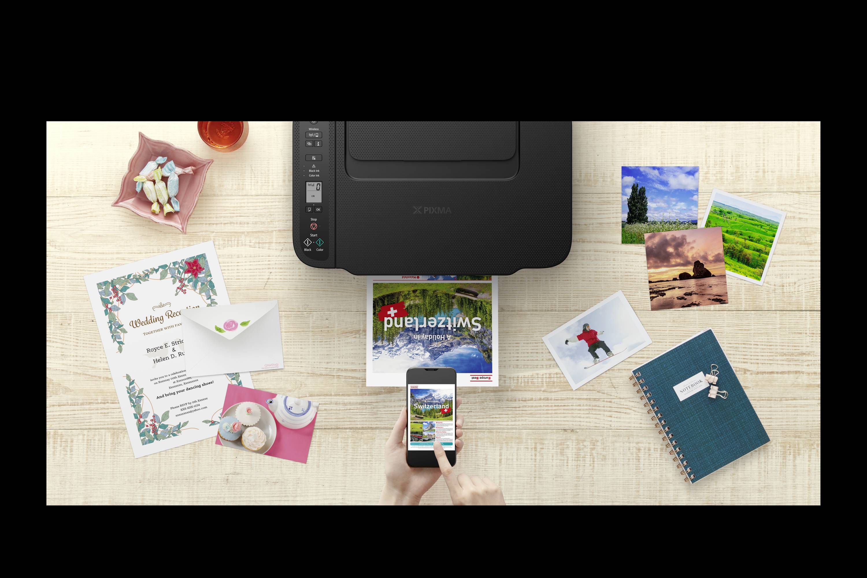 Drucker auf einem Tisch, umgeben von Fotos, einer Hochzeitseinladung, einem Notizbuch und einem Smartphone, das ein Foto druckt.