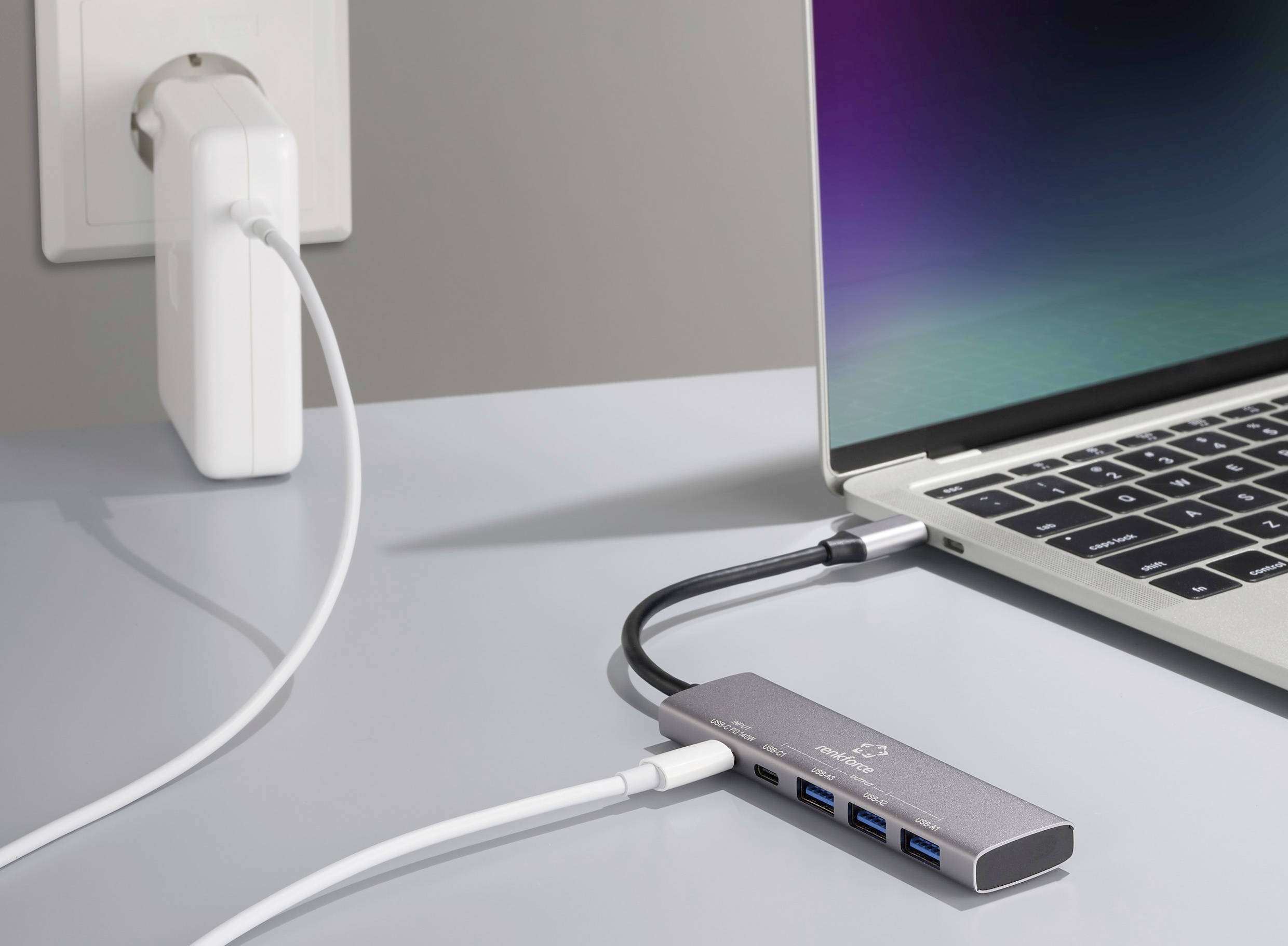 Laptop verbunden mit einem USB-C-Hub, der an eine Steckdose angeschlossen ist. Der Hub hat mehrere Anschlüsse, darunter USB-Ports.