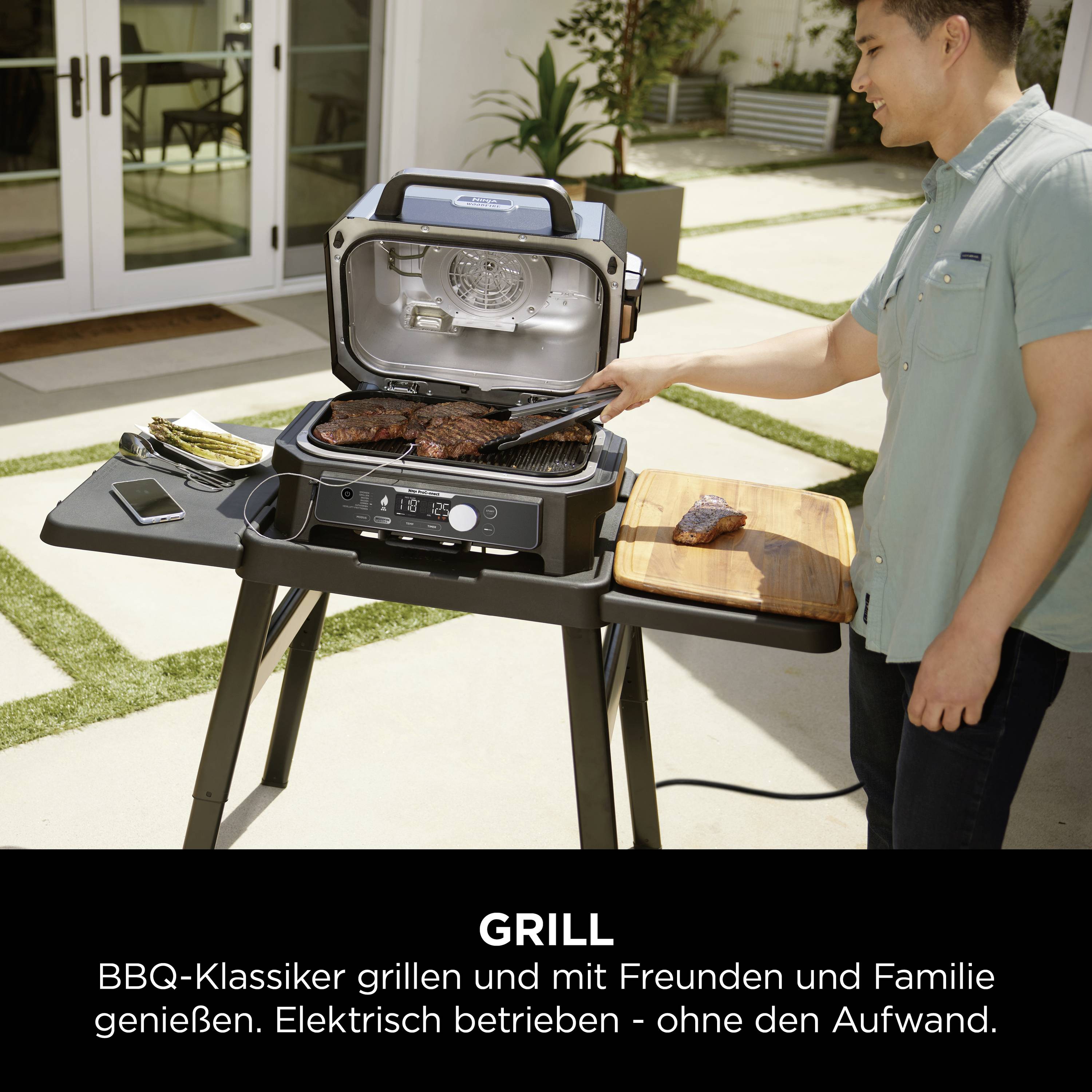 Eine Person steht neben einem Elektrogrill im Garten. Grillgut liegt auf dem Grill und einem Schneidebrett daneben. Text: 'BBQ-Klassiker grillen mit Freunden und Familie genießen'.
