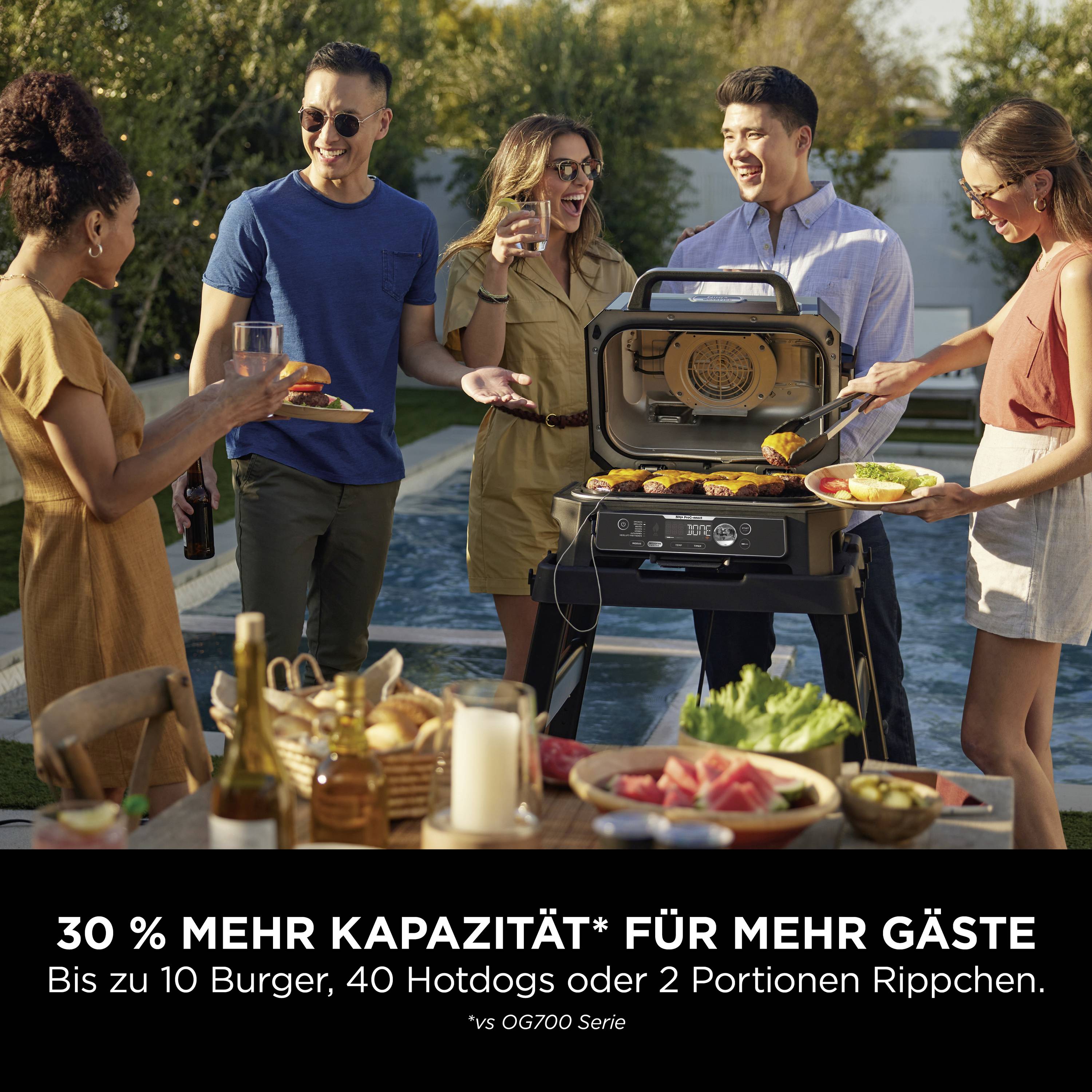Gruppe von fünf Personen bei einer Sommerparty im Garten, grillen auf einem modernen Gasgrill, lachen und heben Gläser an.