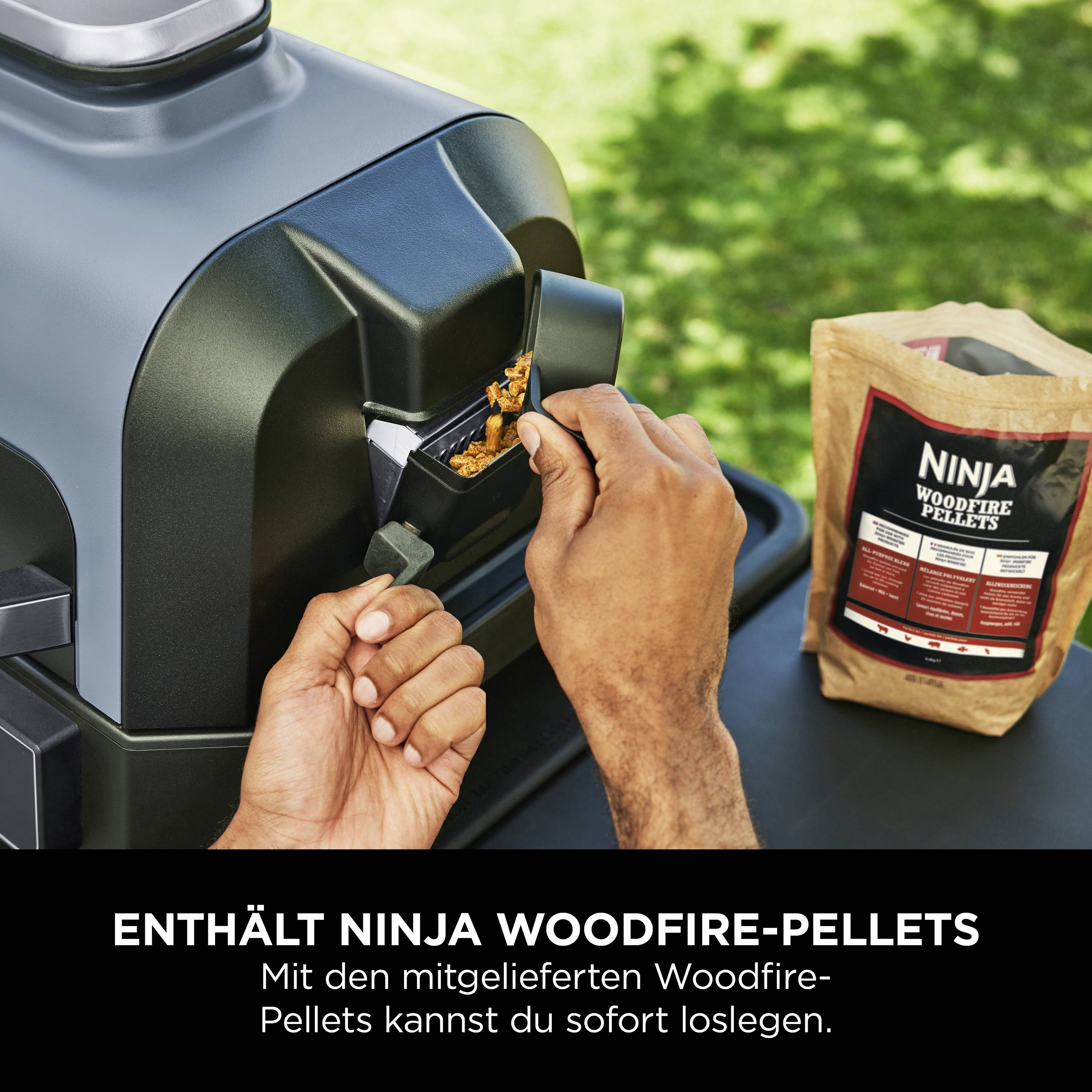 Hand füllt Ninja Woodfire-Pellets in Grill. Beutel mit Pellets auf Tisch daneben.